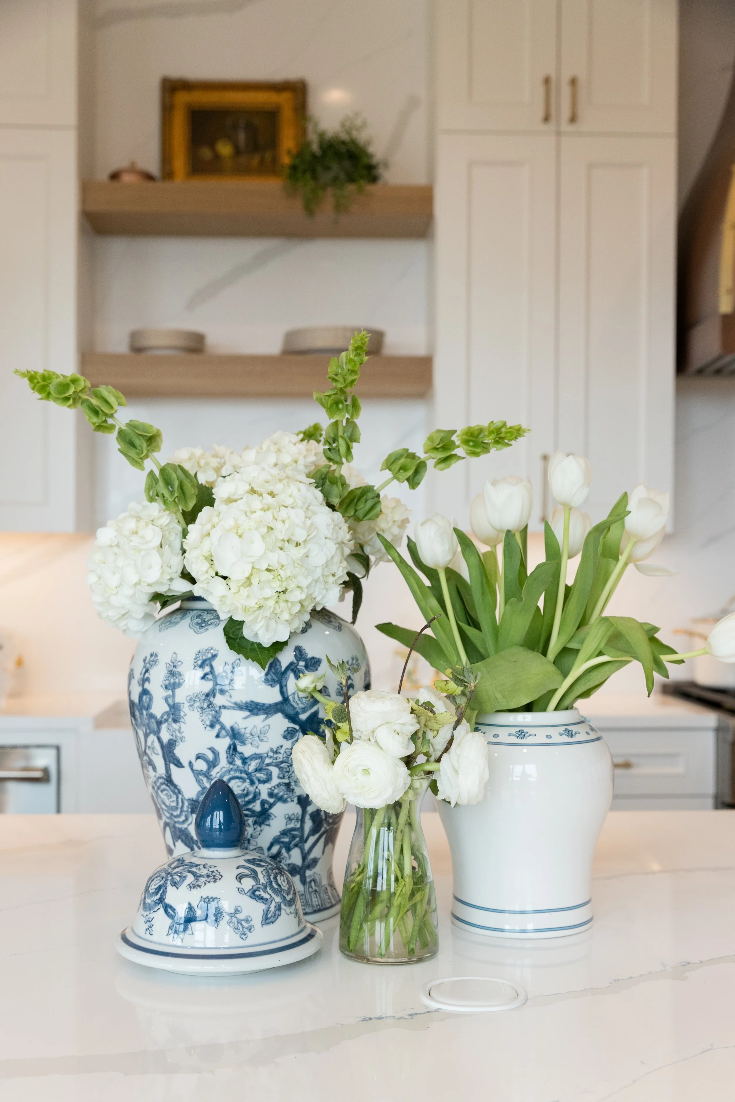 Arrangement of white flowers in blue and white porcelain vases on a white countertop in a kitchen.