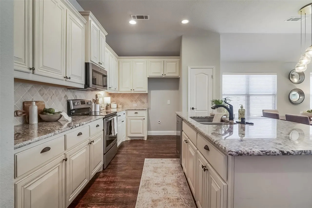 Modern kitchen with white cabinets, granite countertops, stainless steel appliances, hardwood floors, and a kitchen island with a sink and faucet.