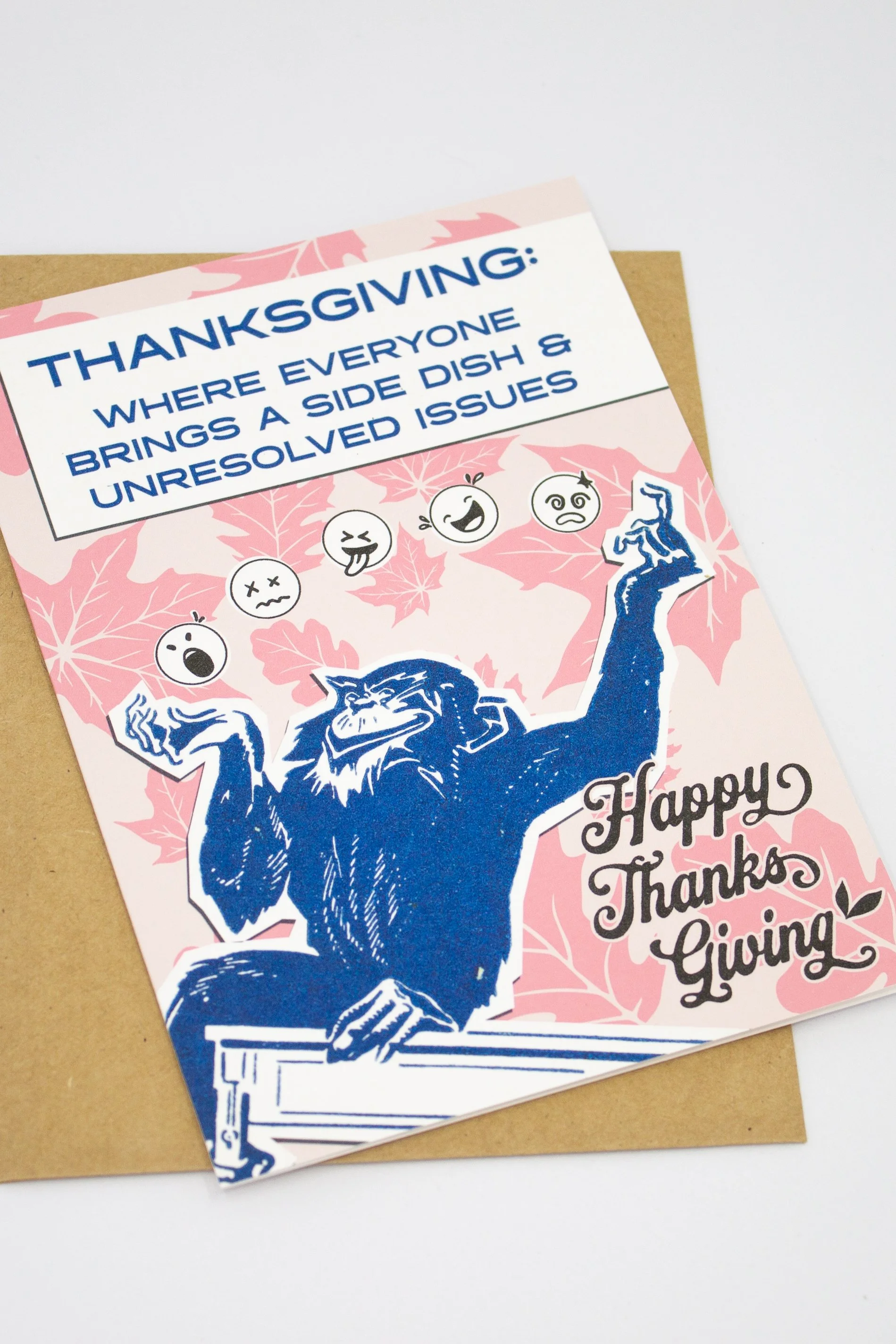This funny Thanksgiving greeting card features a colorful monkey juggling a collection of emoji faces, capturing the emotional balancing act that is Thanksgiving dinner.