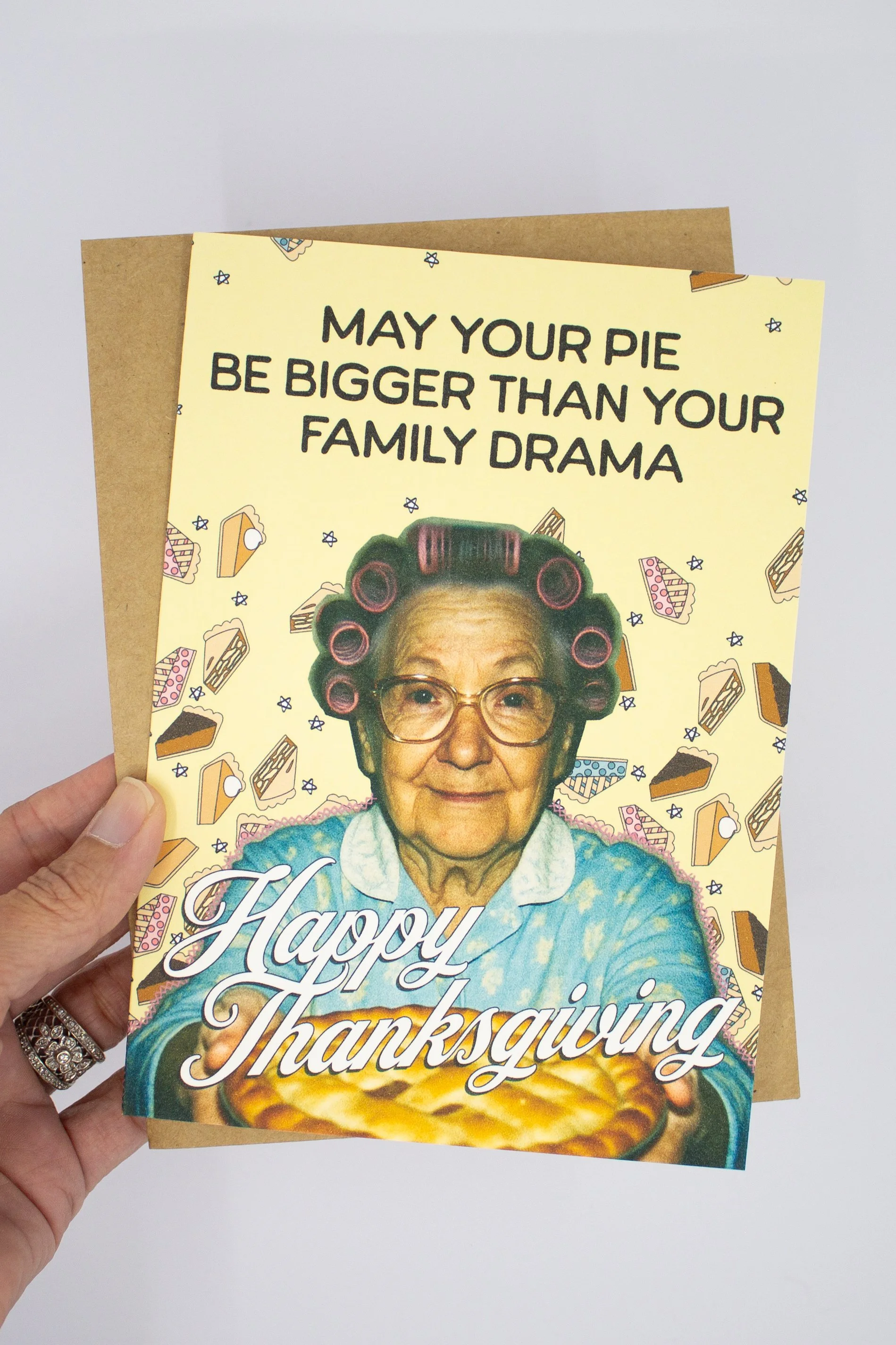 This funny Thanksgiving greeting card features a sweet vintage grandma proudly presenting a homemade pie with the delightfully optimistic wish: "May your pie be bigger than your family drama."