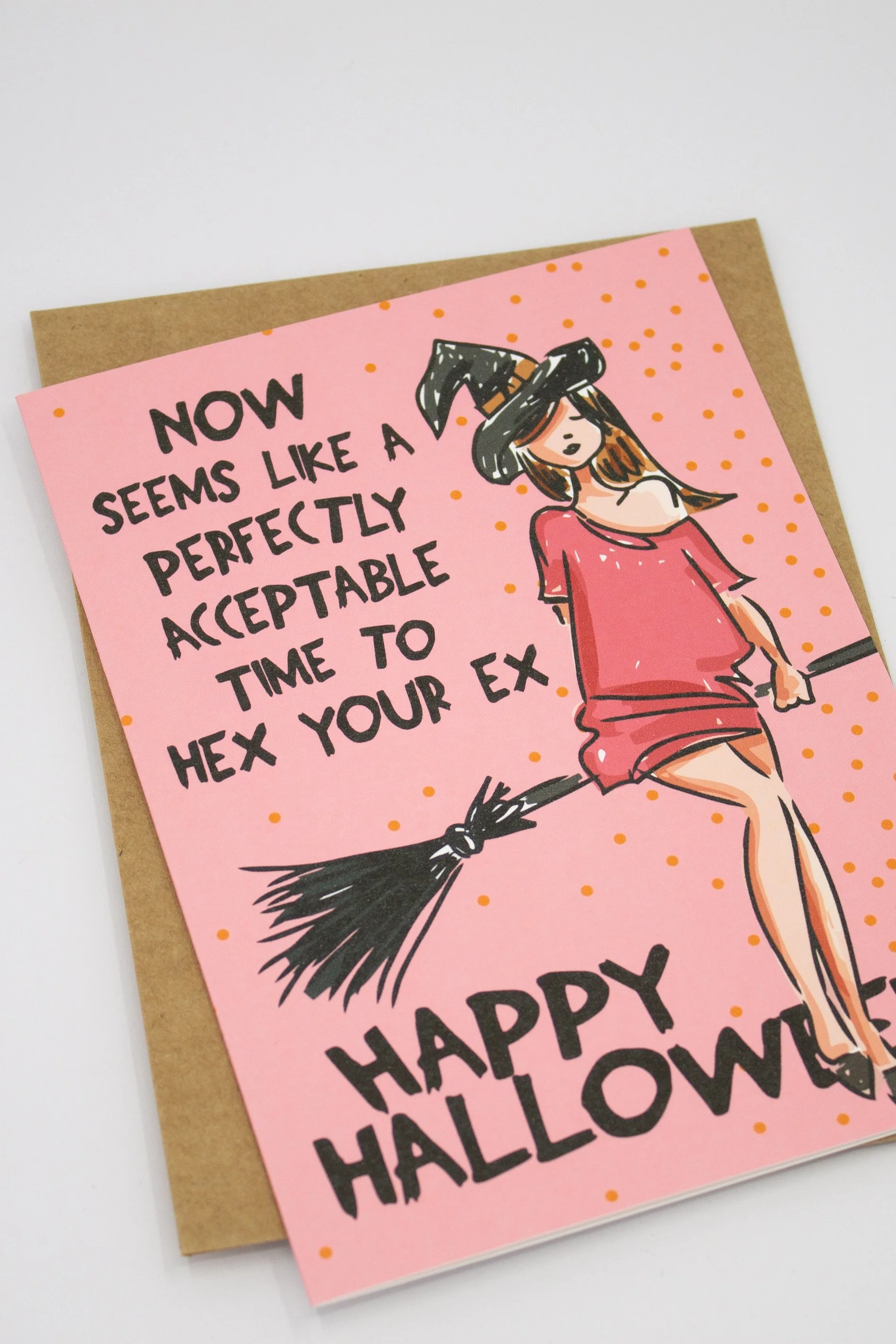 Halloween greeting card featuring a cute witch on her broom against a playful pink background with orange dots.
