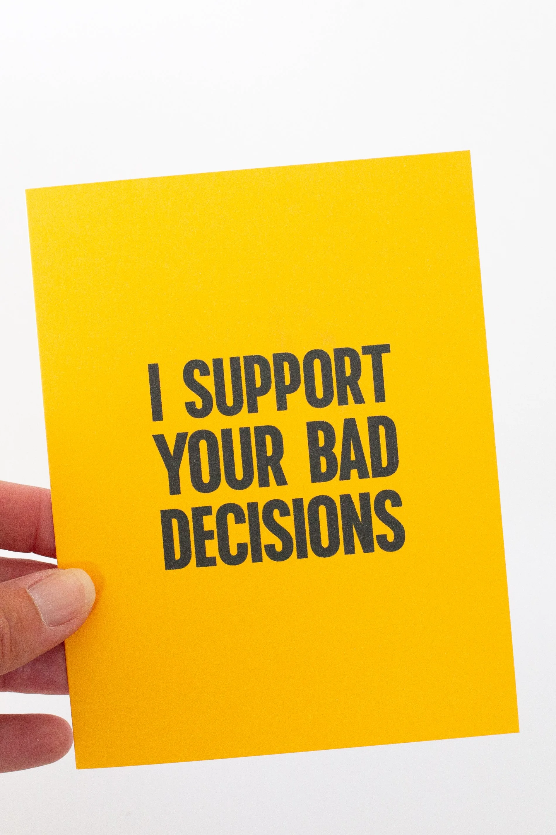 The front is a bold, yellow text-only phrase: “I support your bad decisions.” Enabling? Maybe. Supportive? Definitely.