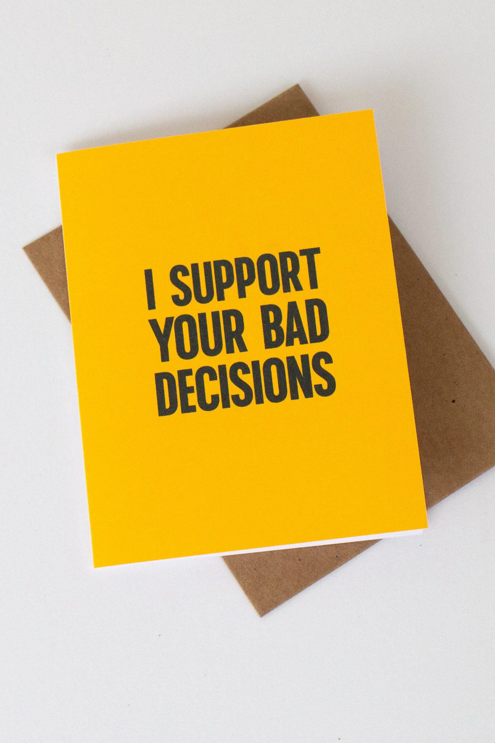 The front is a bold, yellow text-only phrase: “I support your bad decisions.” Enabling? Maybe. Supportive? Definitely.