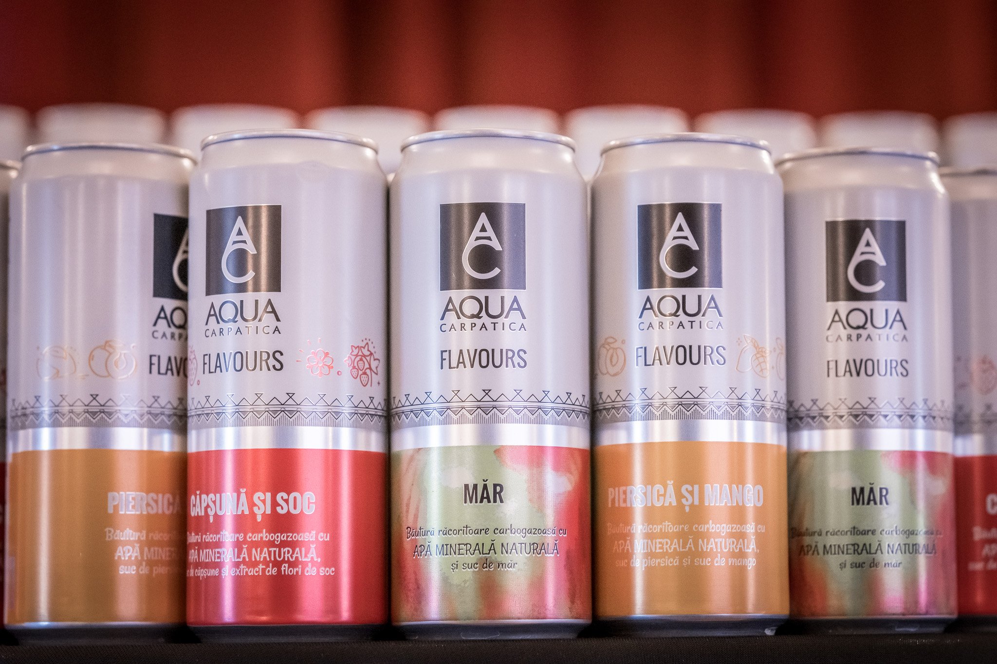 Cans of Aqua Carpatica flavored mineral water with fruit and berry flavors on a store shelf.