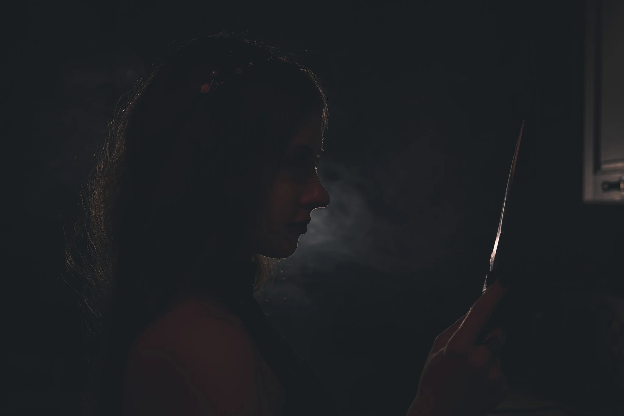 Silhouette of a woman with long hair looking at a mobile device in a dimly lit room.