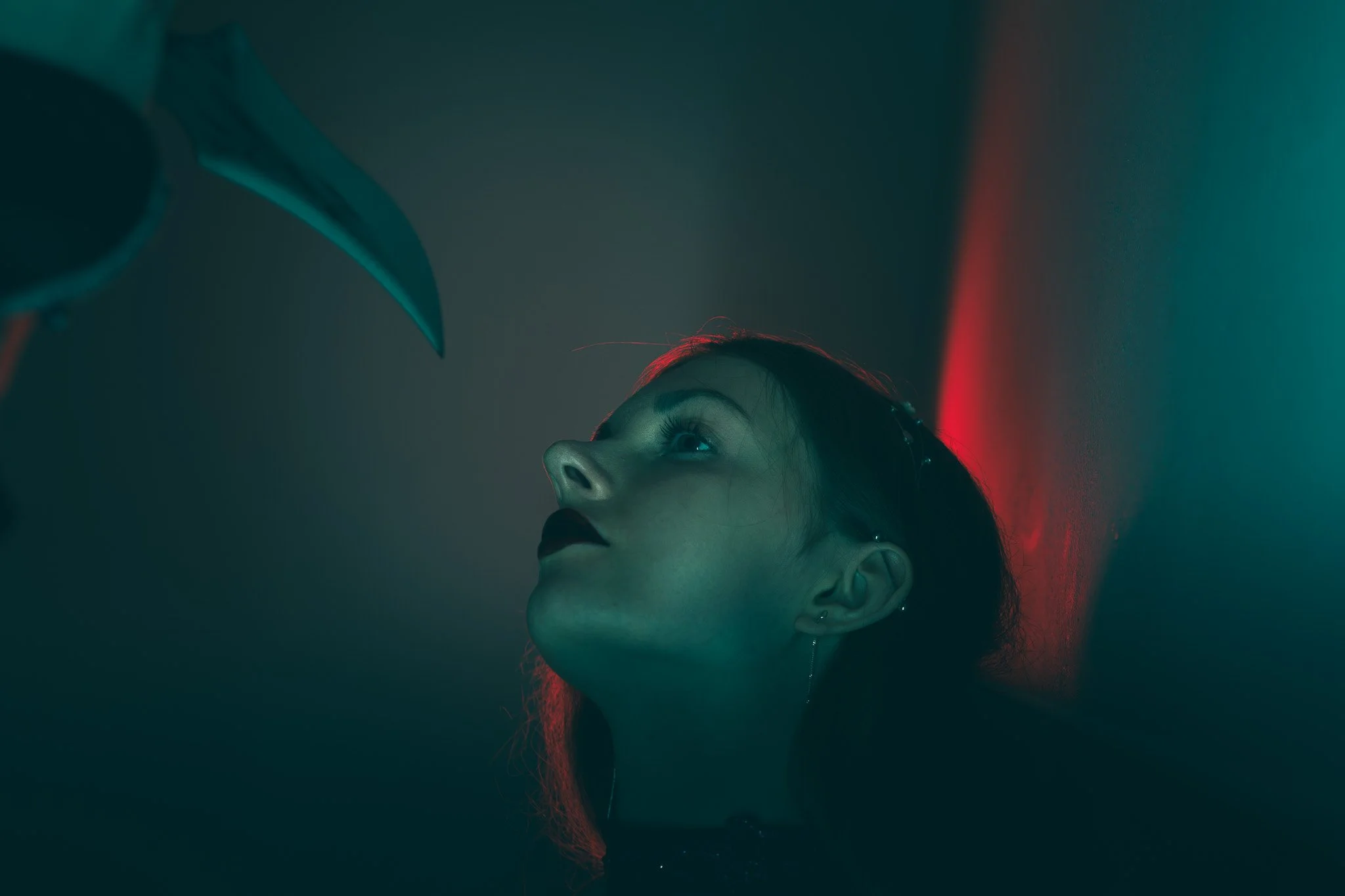 Close-up of a woman with red hair looking upward in a dark room with colored lighting.