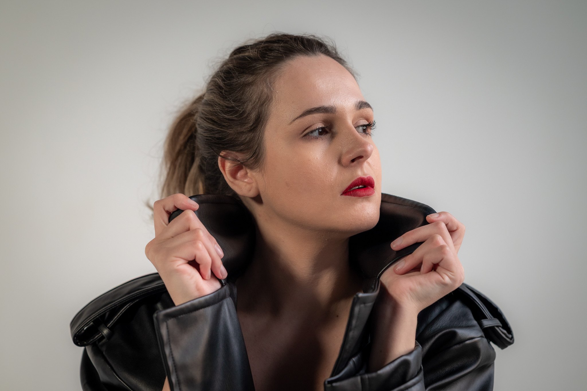 Woman with tied-back hair wearing a black leather jacket, looking to the side, against a light background.