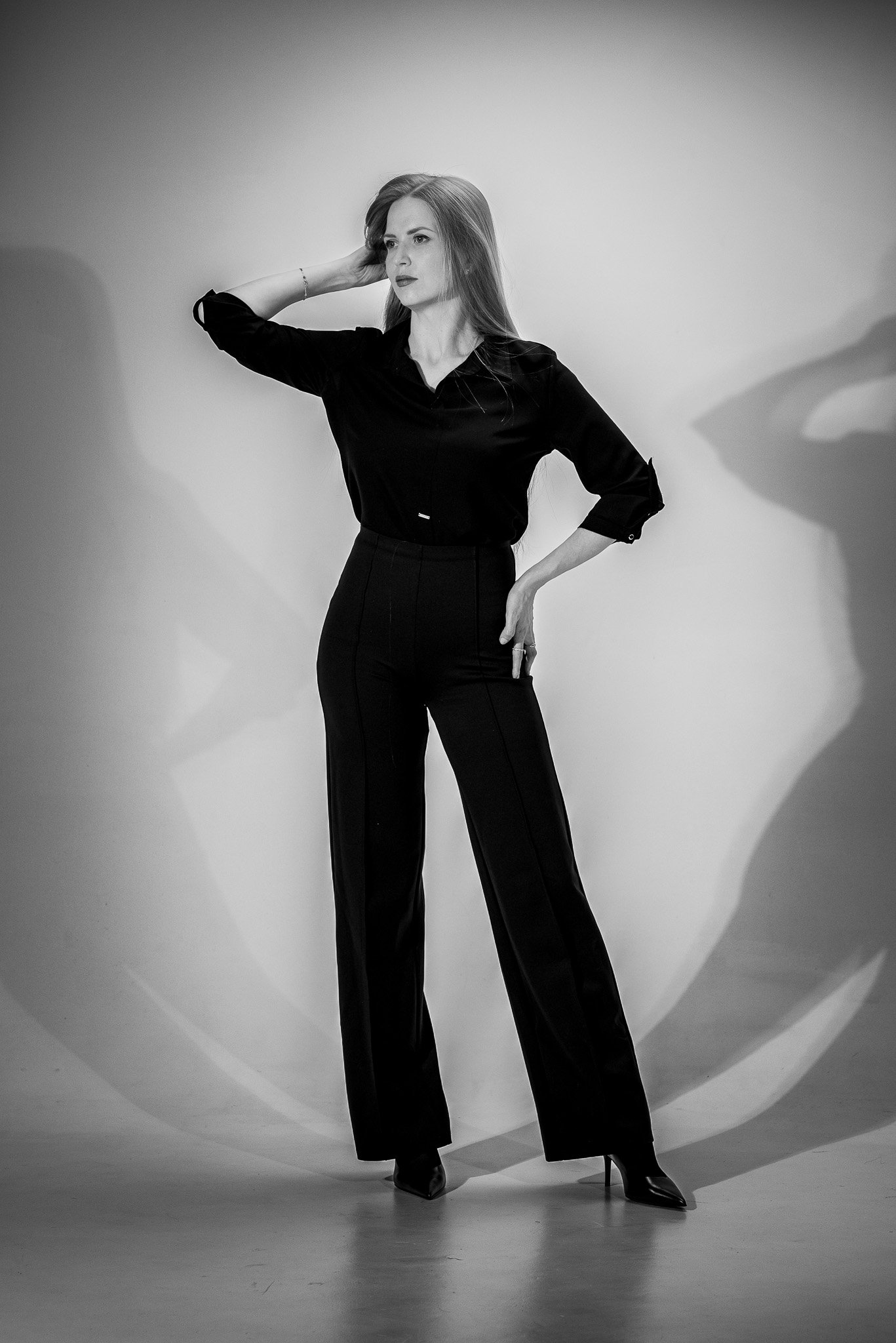 Black and white photo of a woman posing in a studio, wearing a black outfit with high-waisted pants.