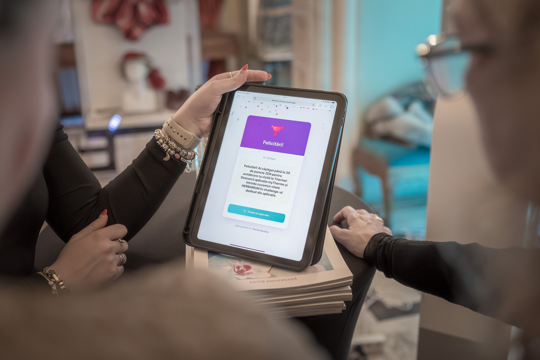 Two women sitting at a table; one is holding a tablet displaying a quiz results page with a purple and white interface, congratulating the user on earning 30 points and inviting them to start a new quiz.