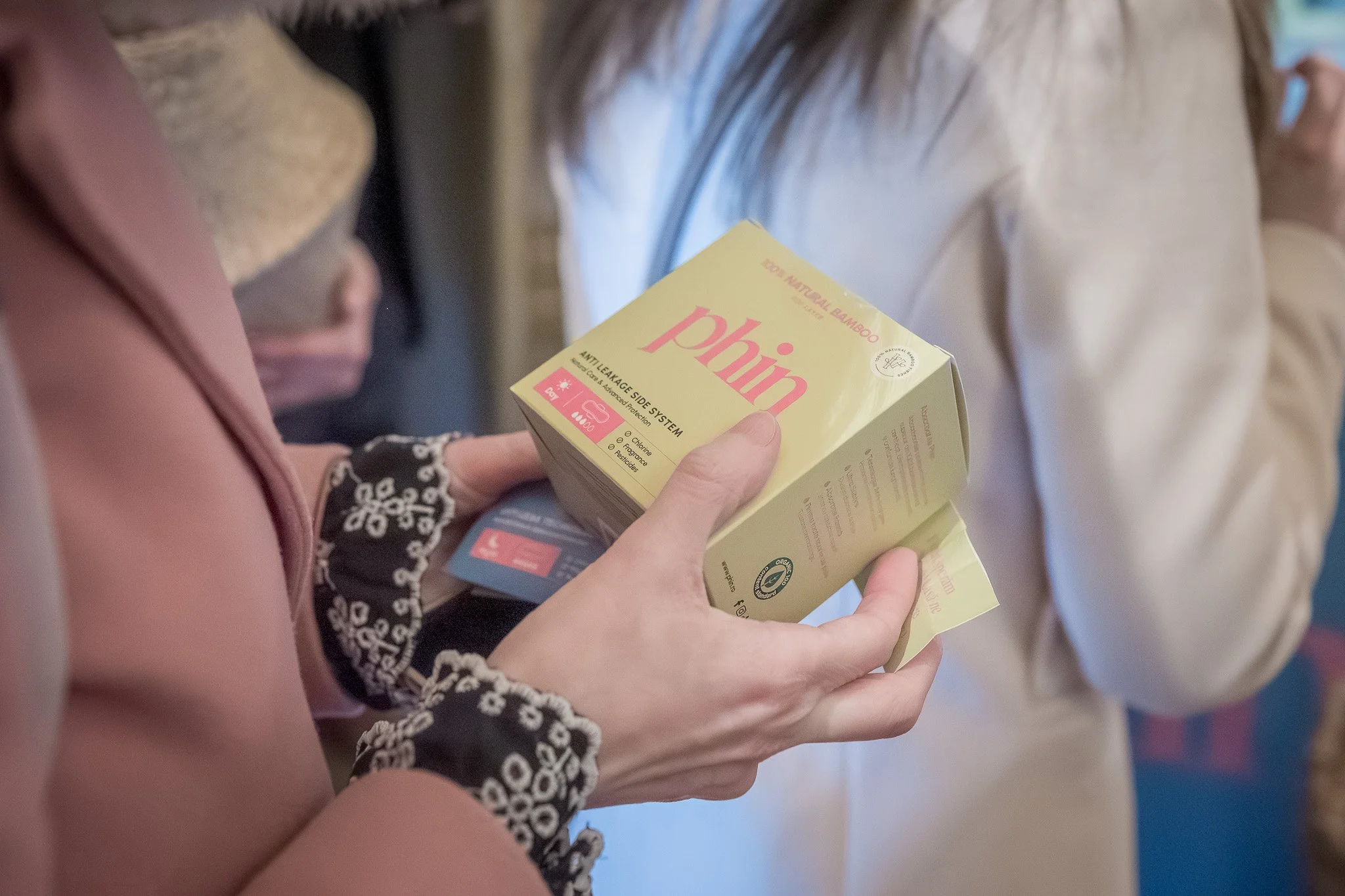 A person holding a yellow box labeled "phiin" containing information about an anti-leakage system, standing next to another person wearing a beige jacket.