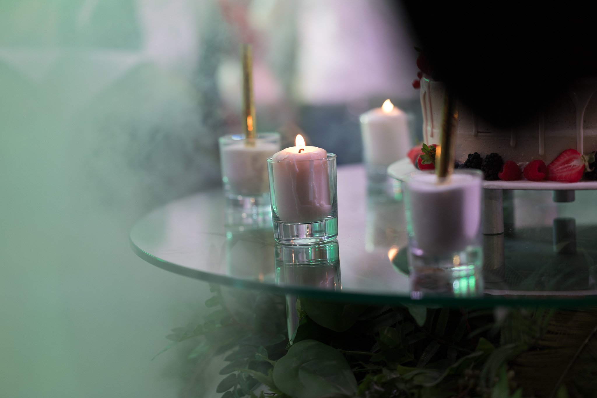 Candles on a glass table with a cake decorated with strawberries and blackberries in the background. Fotograf Praha