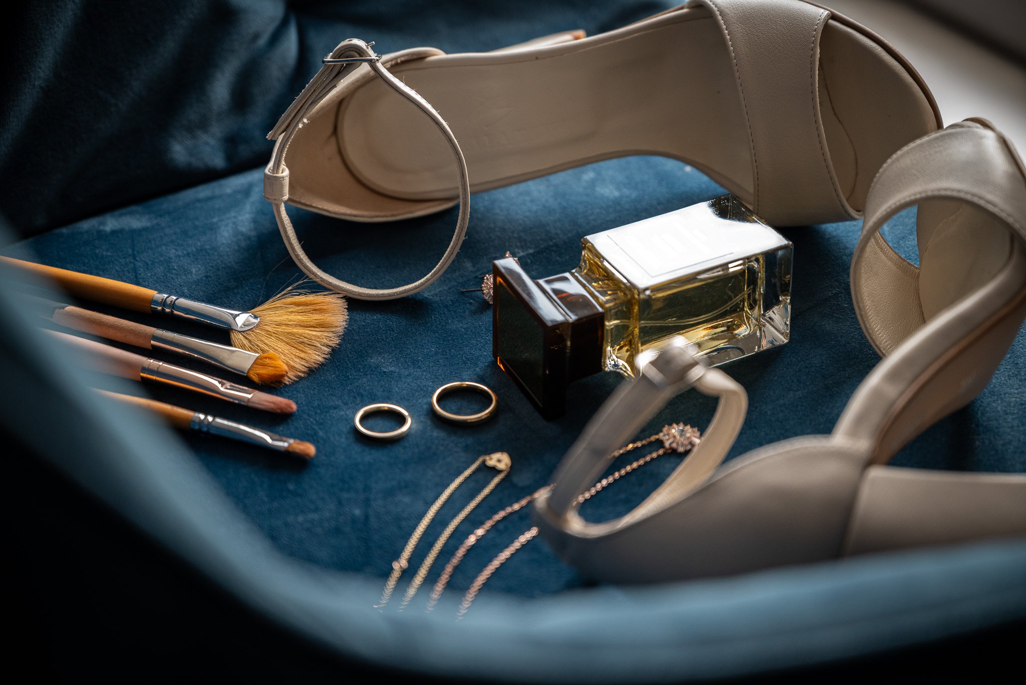 Kolekce šperků, štětců na make-up, flakón parfému a pár béžových lodiček na tmavě modré látce