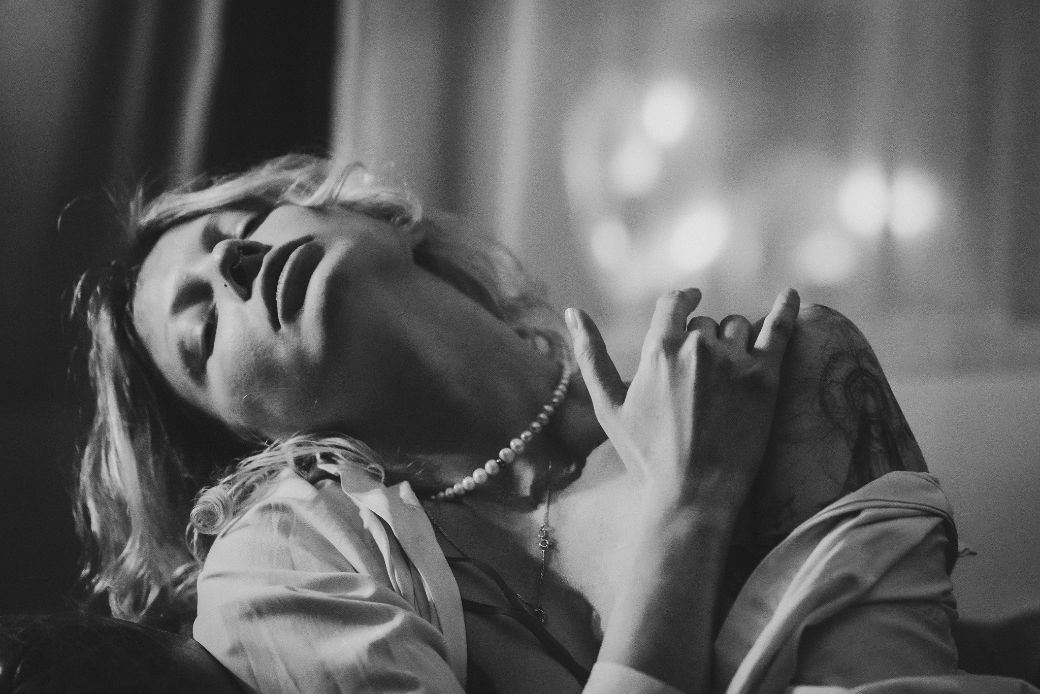 Black and white portrait of a woman with a pearl necklace, eyes closed, head tilted back, and hands on her shoulders.