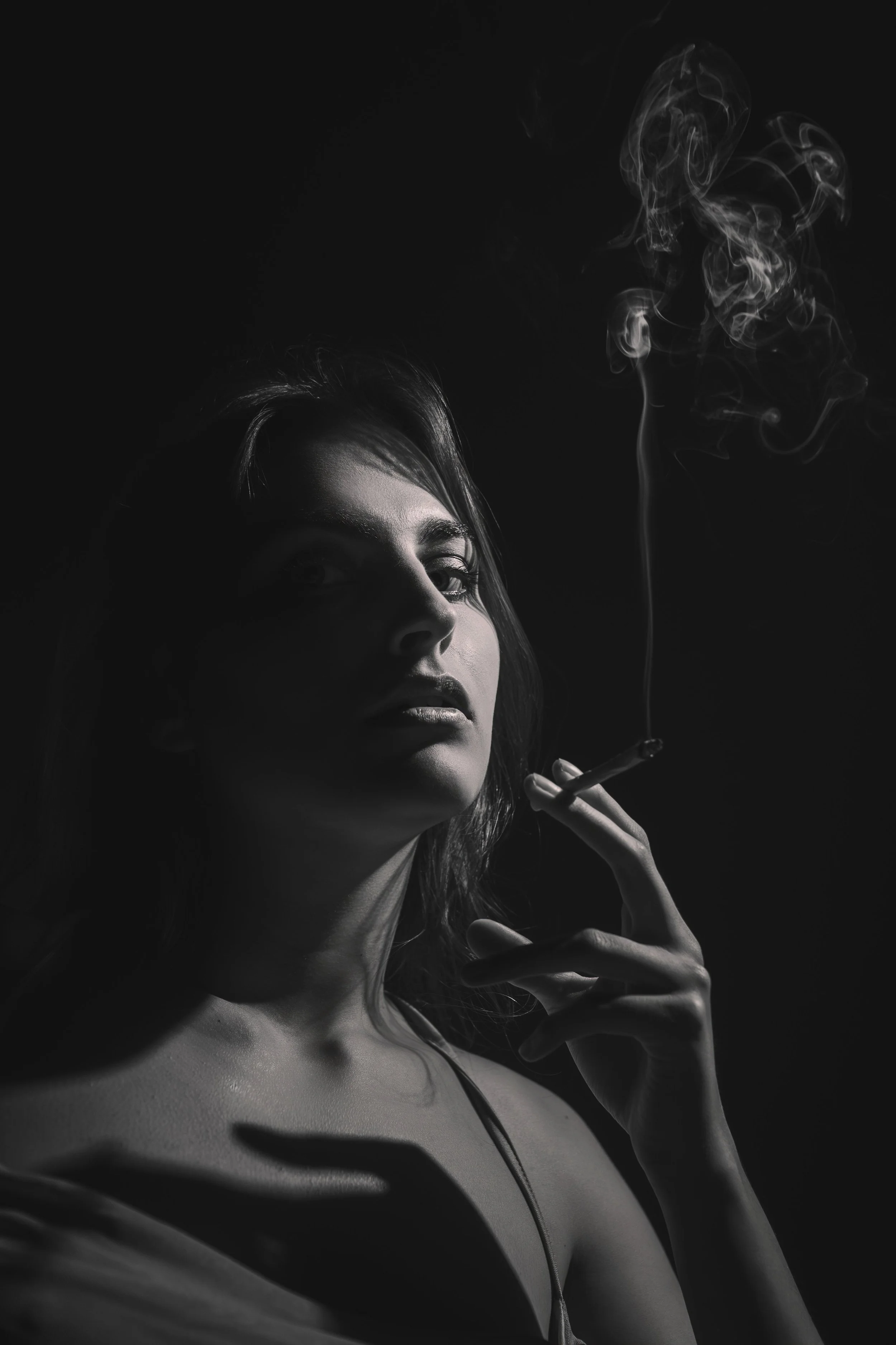 Černobílá fotografie české ženy s dlouhými vlasy, která drží cigaretu, z níž stoupá dým. Žena je částečně zakrytá, má stíny na obličeji a krku a zdá se, že se dívá přímo do fotoaparátu.
