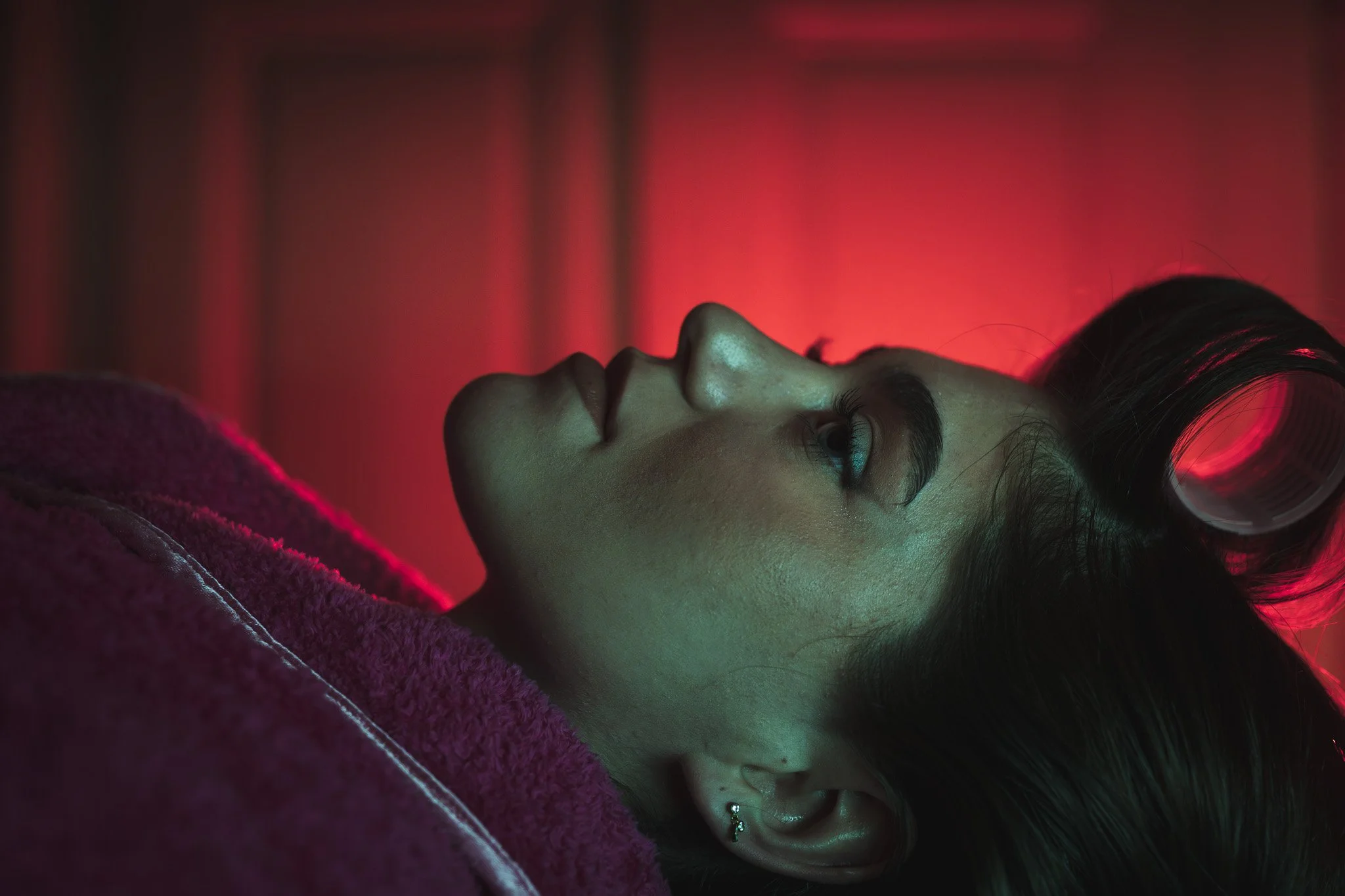 A close-up of a woman lying on her side, illuminated by red and green lights.