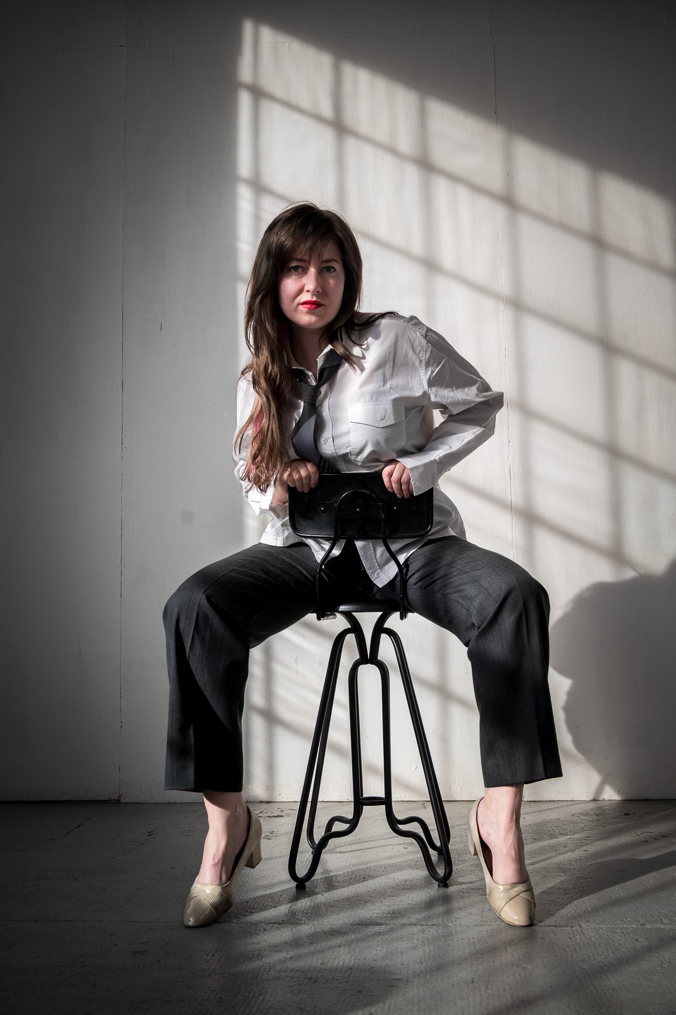 Person sitting on a stool in a white shirt and tie.