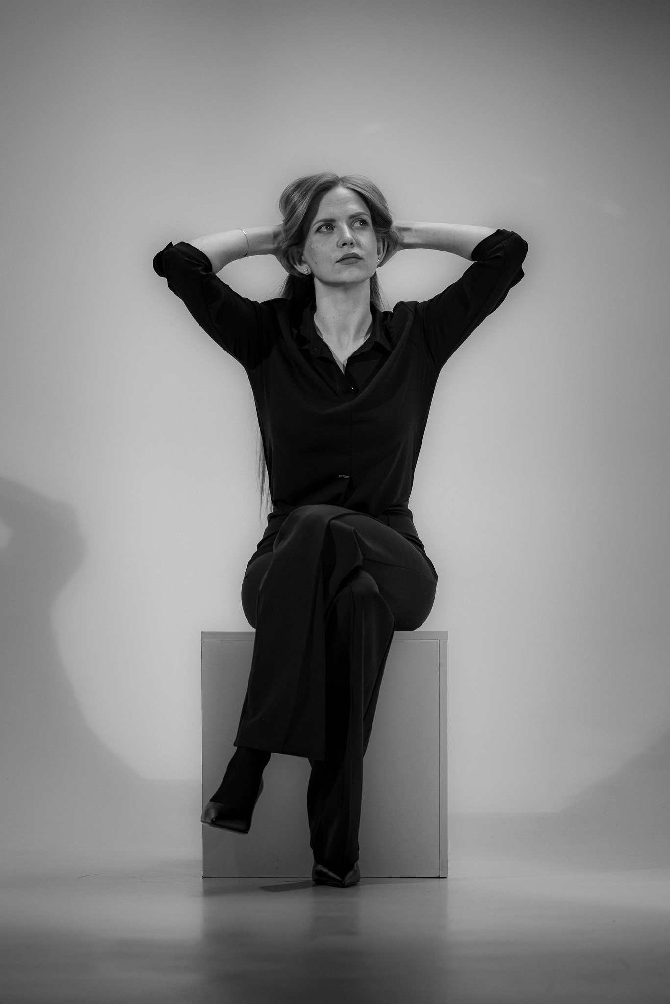 Black and white photo of a woman sitting on a box with legs crossed, hands behind her head.