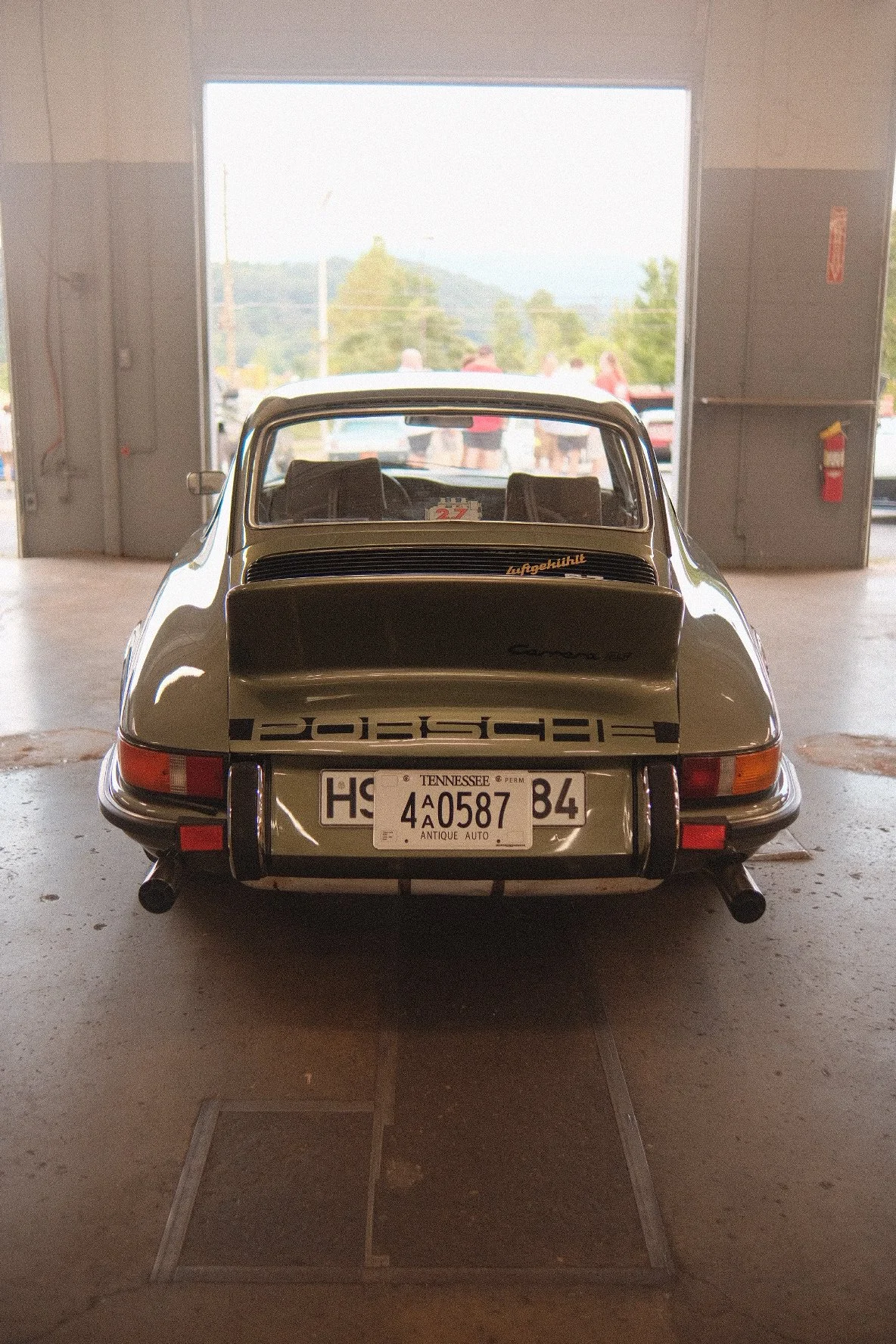 rear view of a vintage green Porsche 911 inside a garage with an open door, showing the license plate from Tennessee, and a scenic background outside.