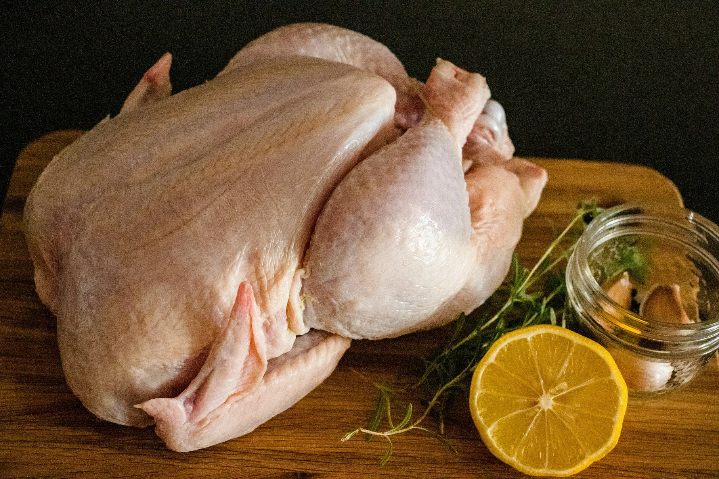 Raw whole chicken on a wooden board with lemon and herbs