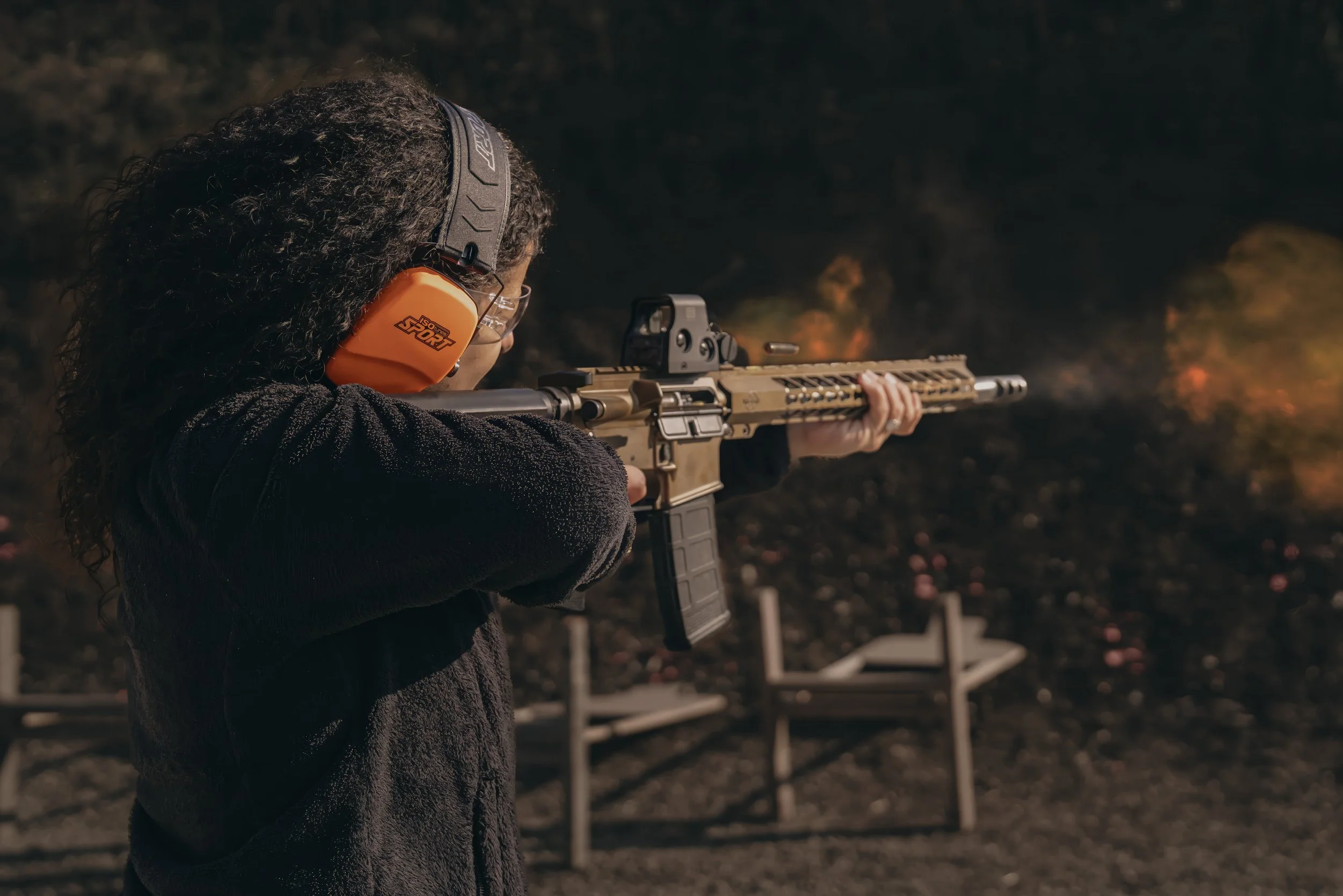 Person wearing ear protection and shooting a rifle at a firing range.