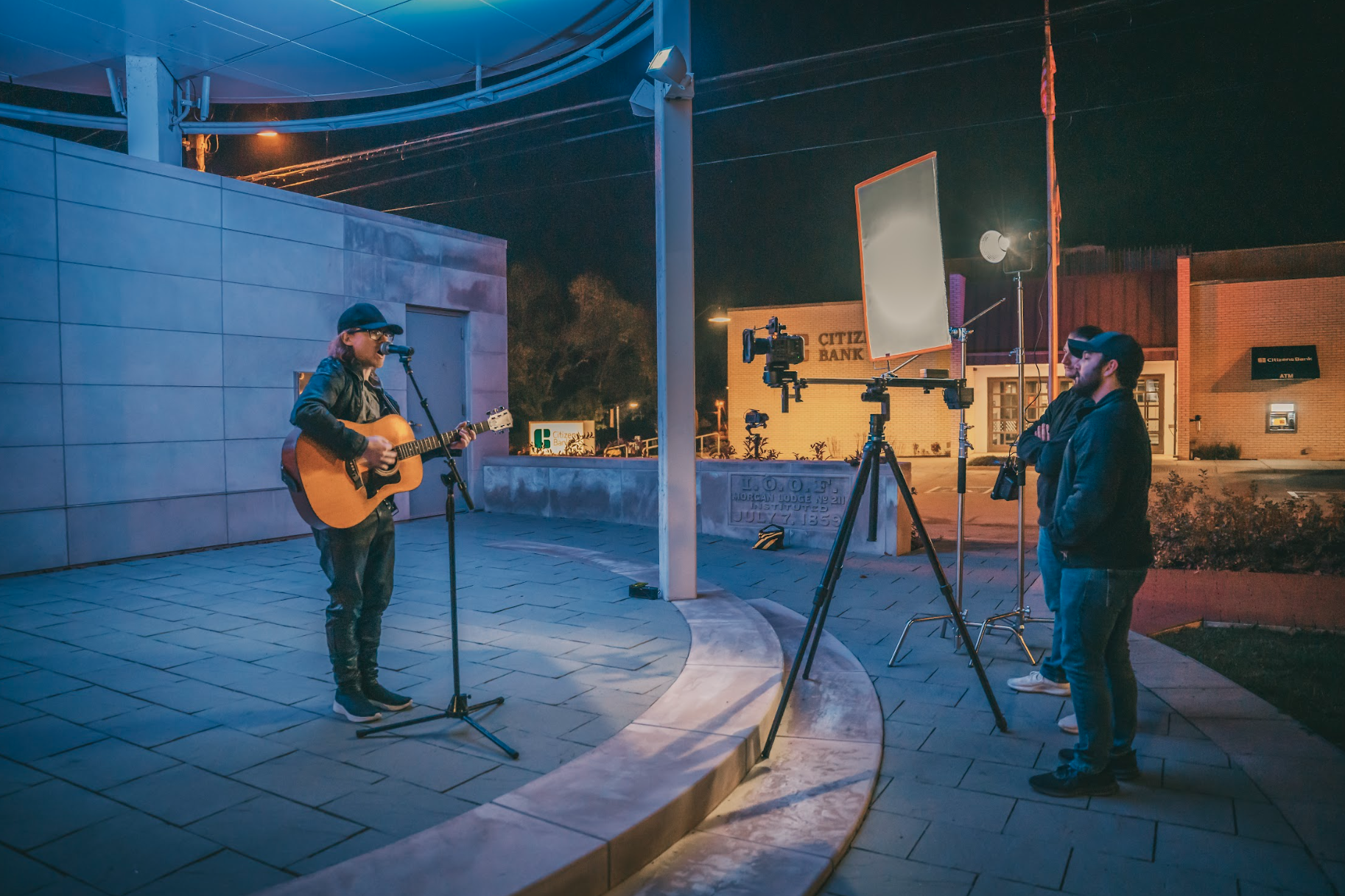 Outdoor musician performance being filmed at night with professional lighting and camera equipment.