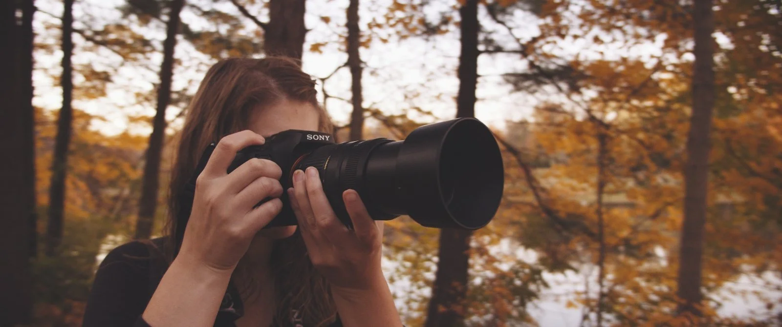Caitlyn Hymer photographing in a forest during fall