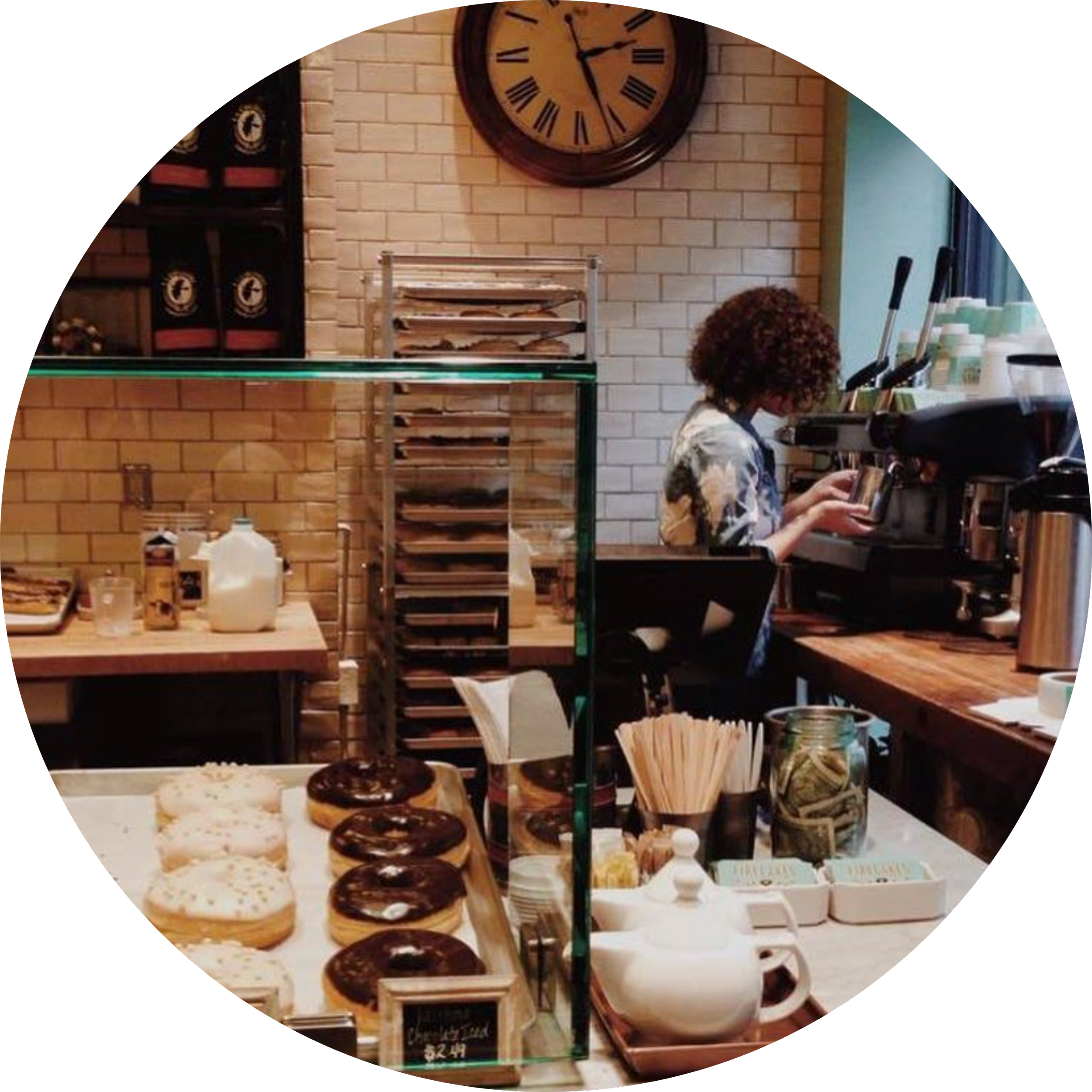 Barista pouring espresso behind a bakery counter displaying breads and pastries.