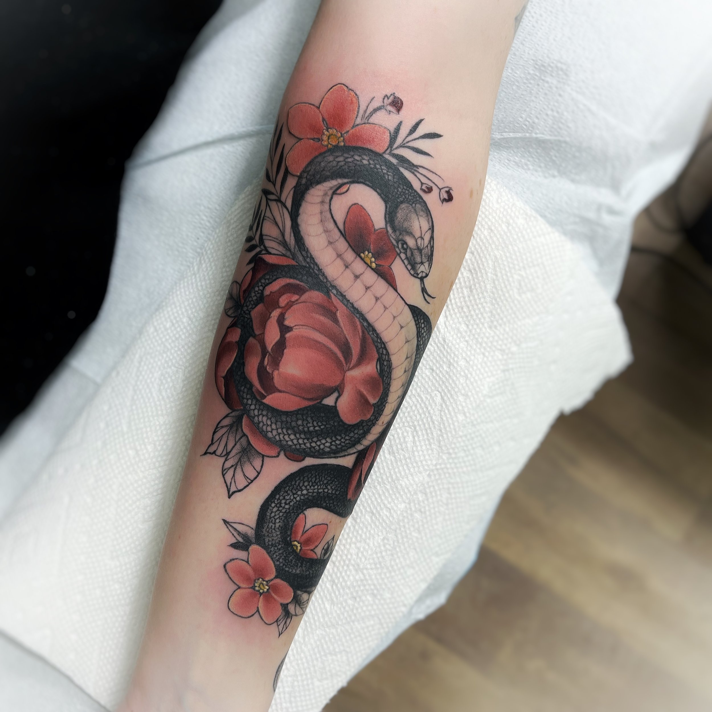 Tattoo of a snake entwined with red flowers on a forearm