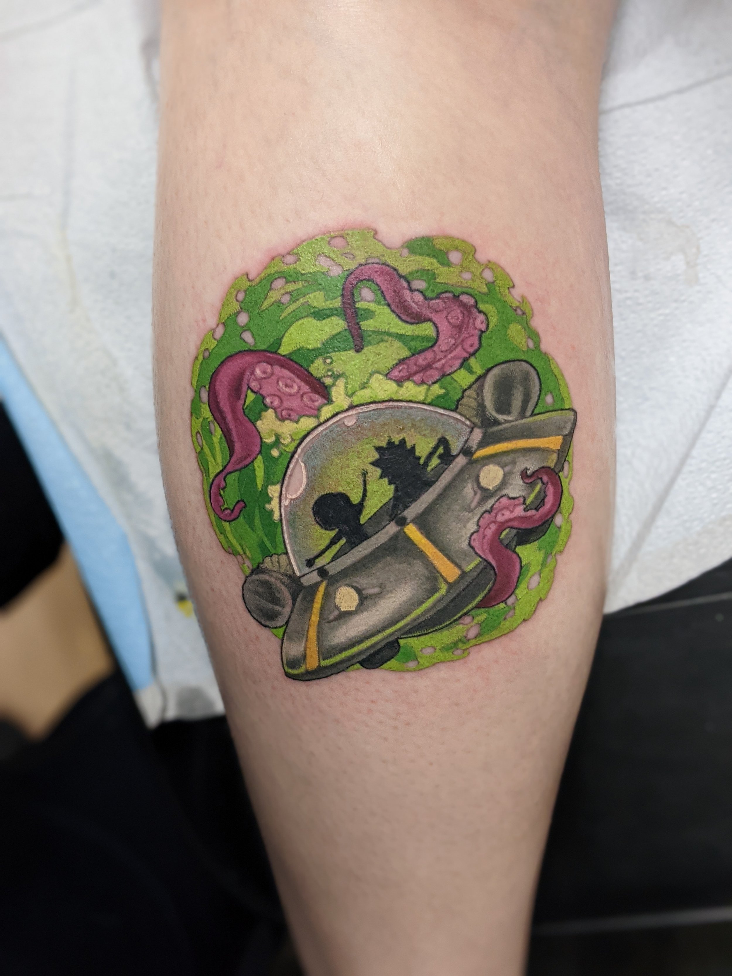Colorful tattoo of a spaceship with creatures in a glass dome, surrounded by green slime and purple tentacles.