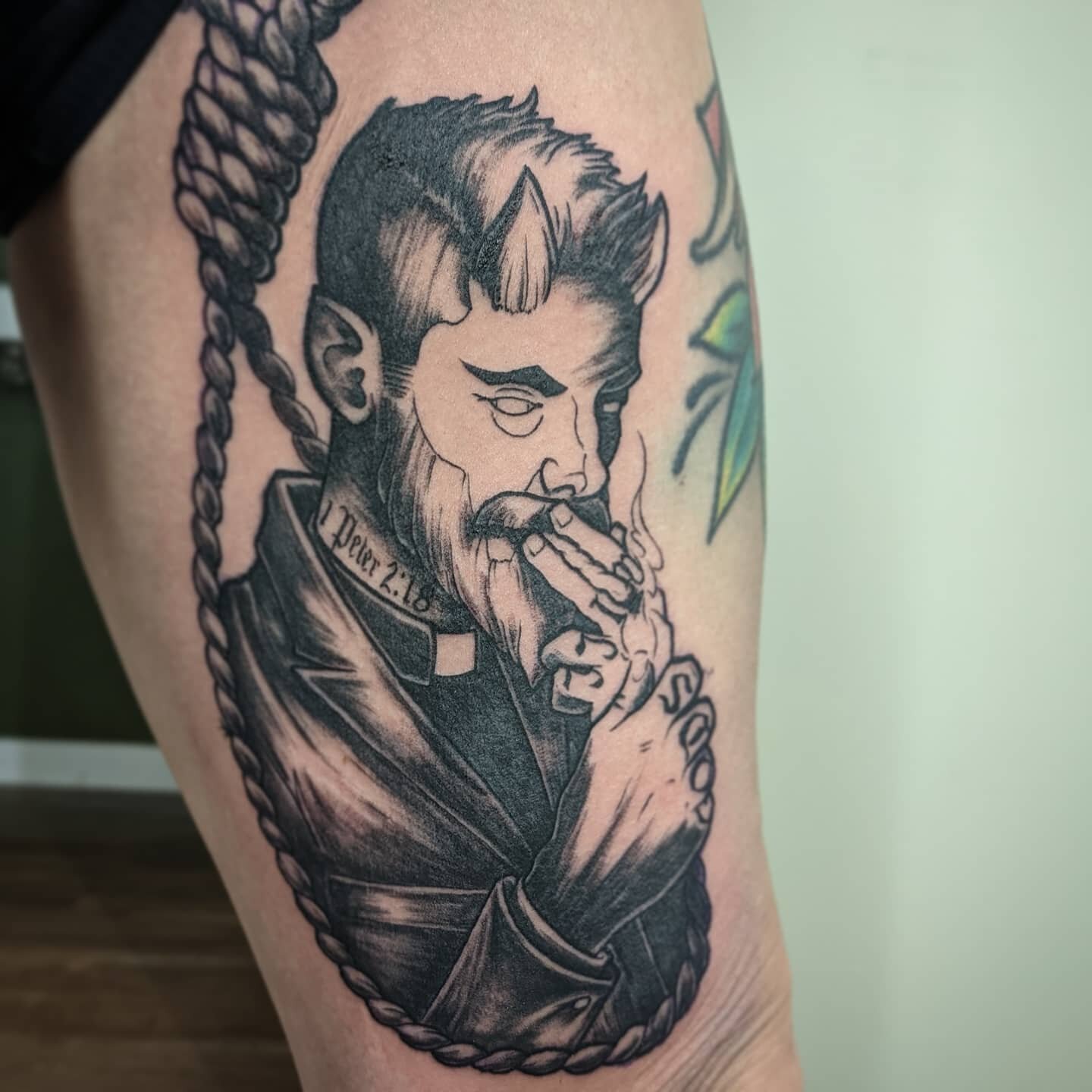 Tattoo of a devilish figure with small horns smoking, wearing a suit with a Bible reference "1 Peter 2:18" on the neck, surrounded by a rope.