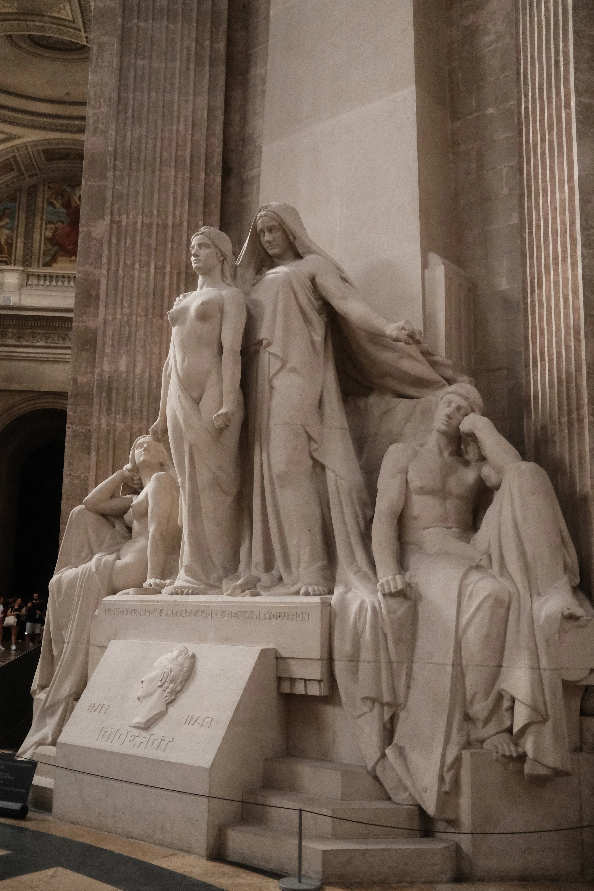 White marble sculpture of four women with historic clothing and hairstyles inside a museum, surrounded by tall Corinthian columns and painted ceiling murals.
