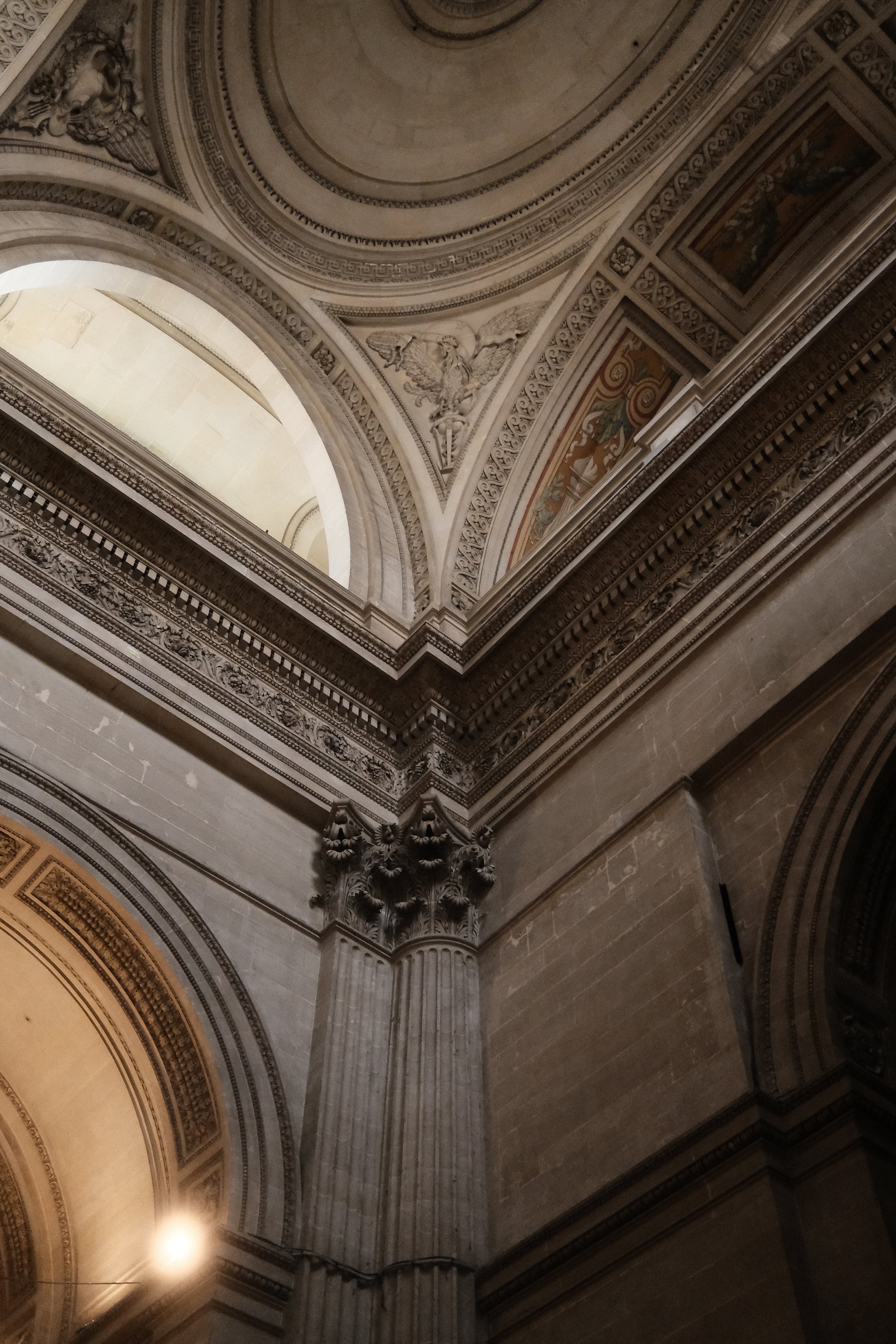 Looking up at ornate marble architectural details, including a large arch, decorative molding, and a column with a detailed capital, within a historic building.