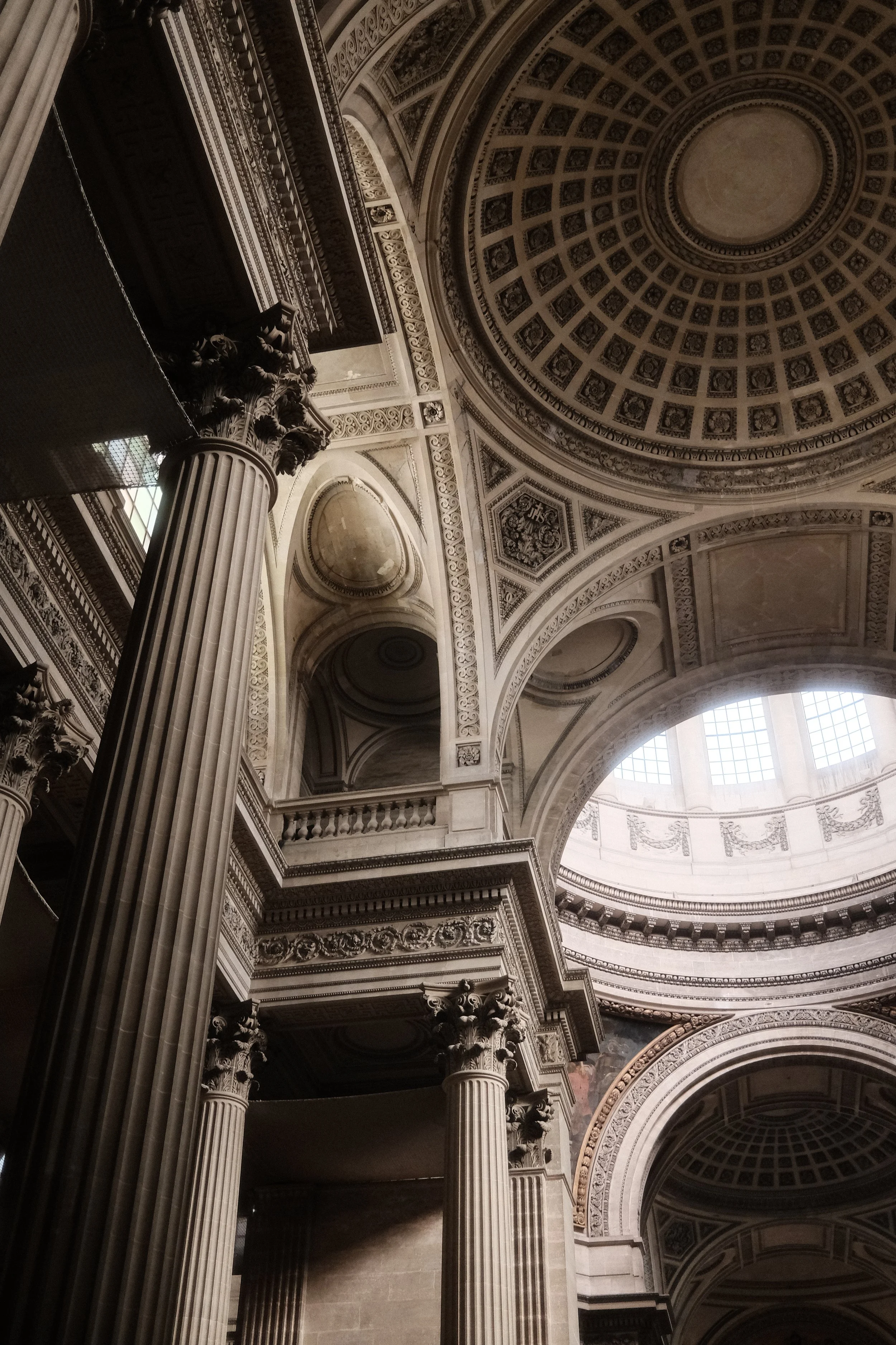Interior view of a grand building with large columns, ornate architecture, and a domed ceiling with detailed patterns and windows.