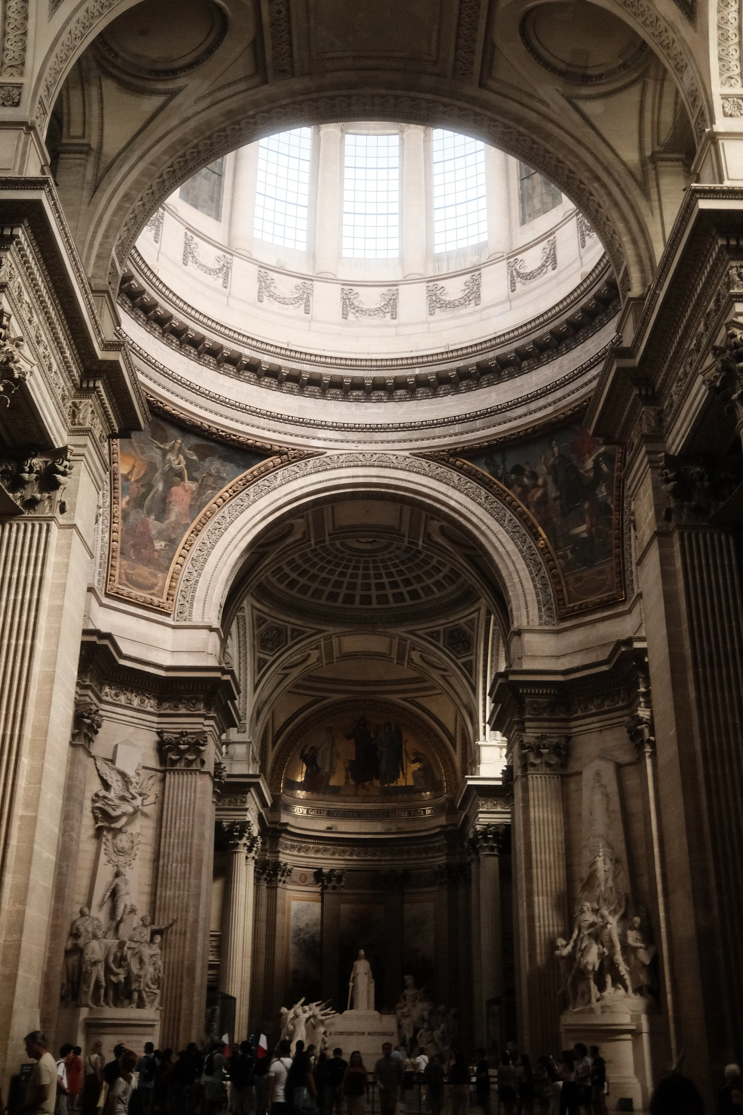 Interior view of a grand historic building with high ornate ceilings, large columns, classical sculptures, and religious paintings, with people gathered inside.