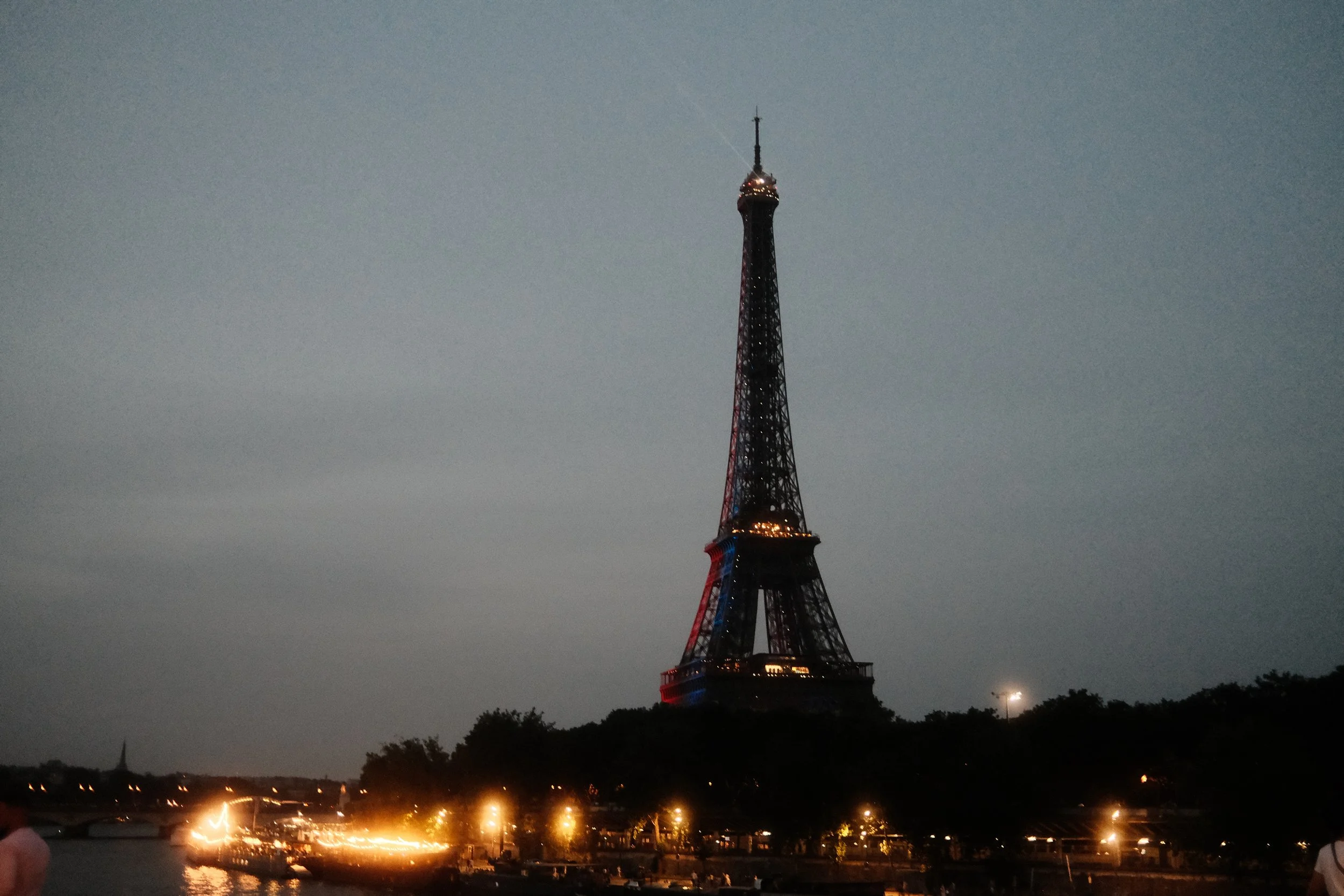 Nighttime view of the Eiffel Tower illuminated, with a river and city lights in the foreground.