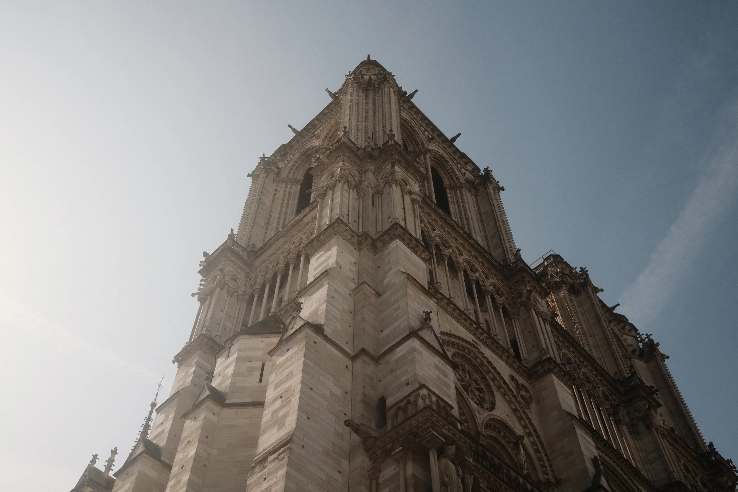 Low-angle view of a historic gothic-style cathedral tower with intricate architectural details against a partly cloudy sky.