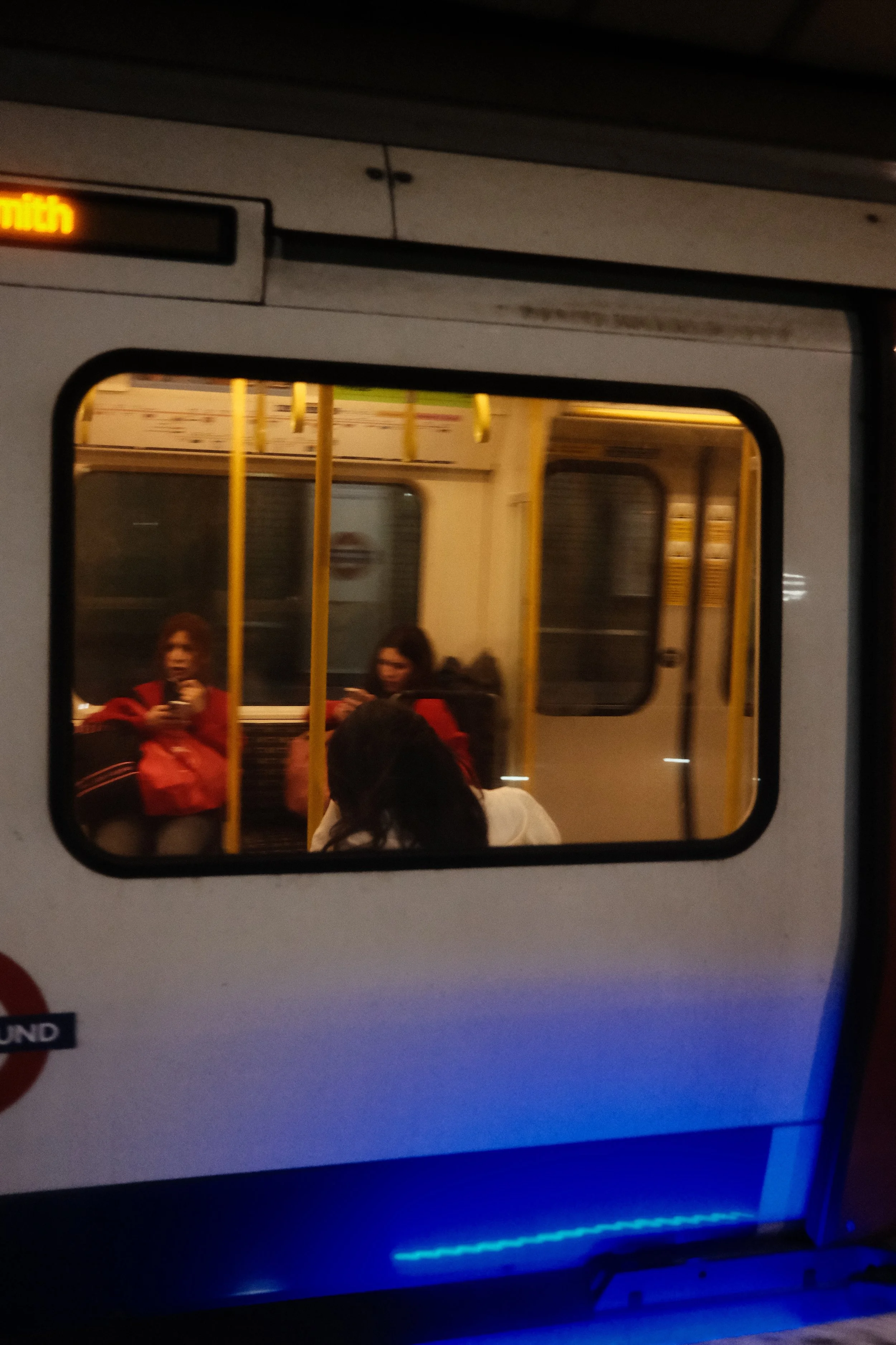 People sitting inside a train and looking at their phones, viewed through the train window at night.