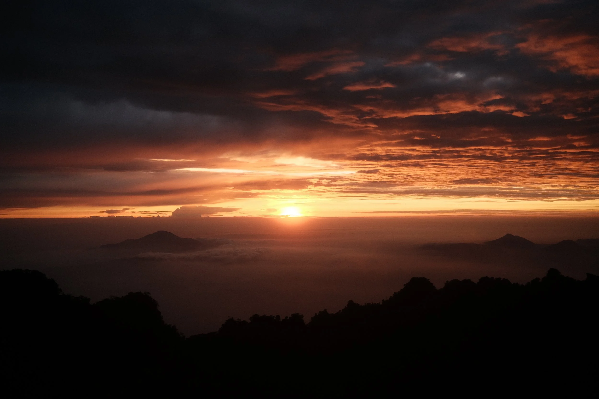 Sunset over mountains with dark clouds and orange hues in the sky.