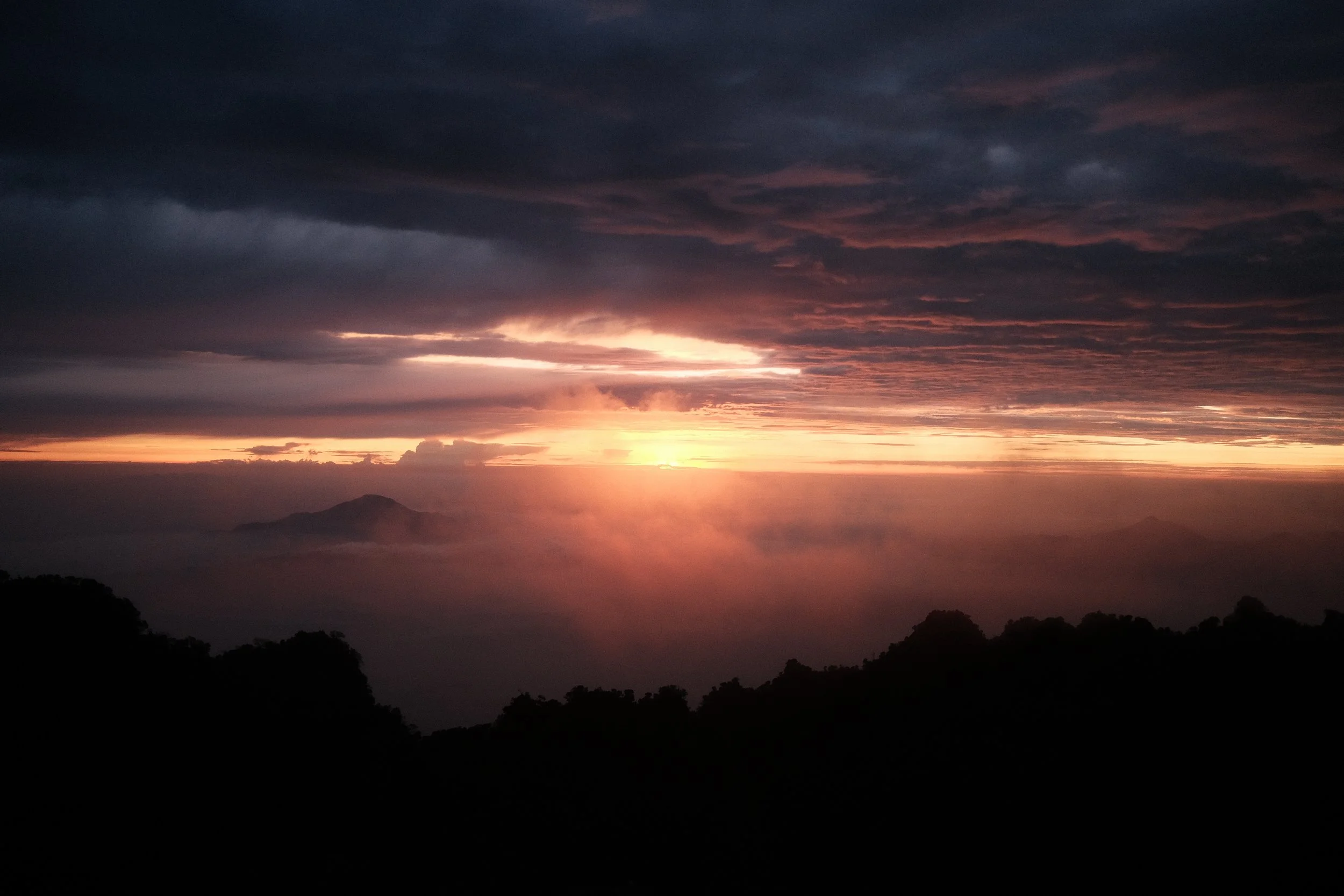 Sunset over a mountain landscape with dark clouds and a horizon glow.