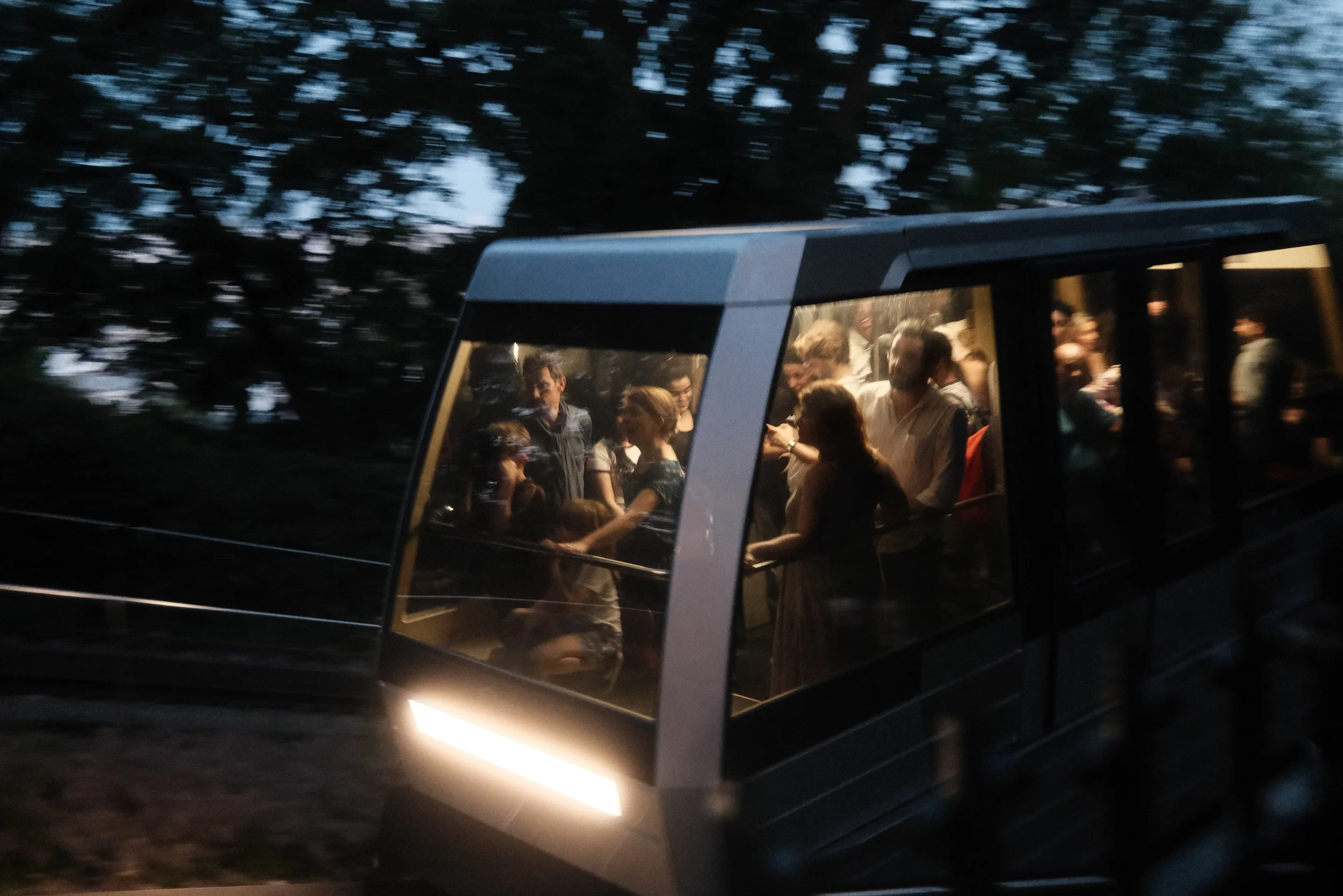 People riding a funicular or cable car at dusk or night, surrounded by trees.