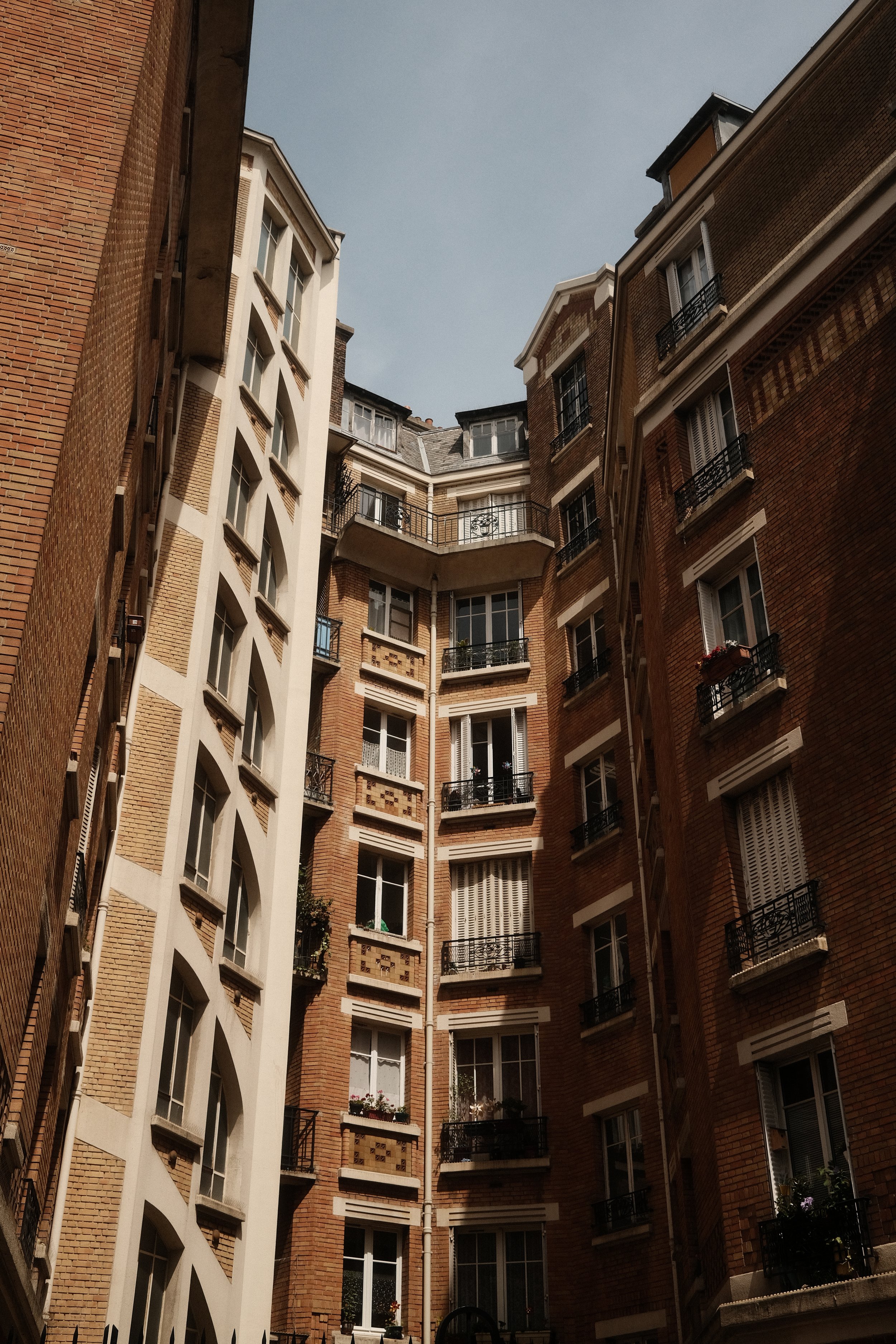 Tall brick apartment buildings with balconies in a narrow courtyard under a cloudy sky.
