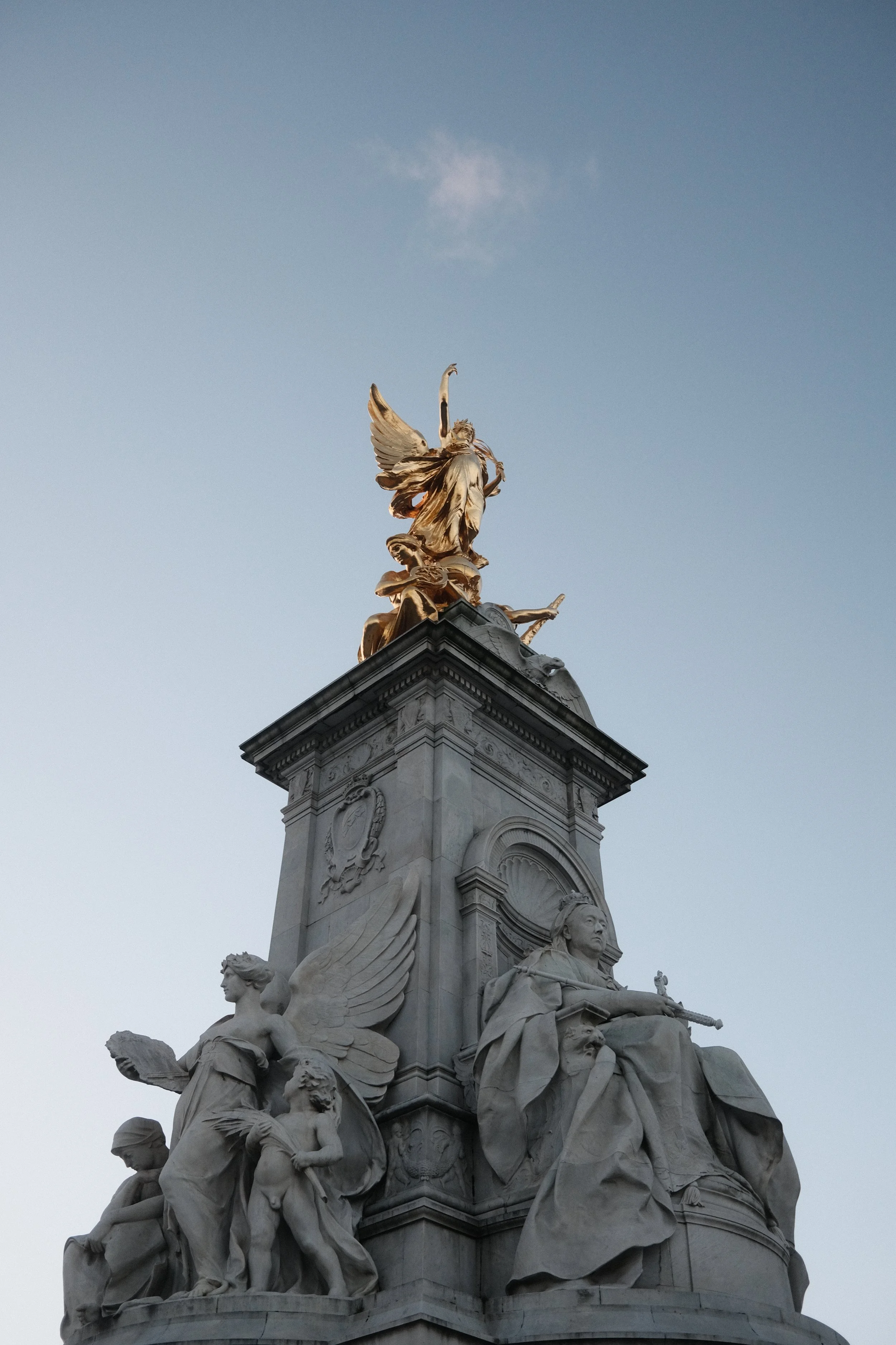 A tall white marble monument with multiple detailed sculptures vaulting off its top, set against a clear sky. The sculptures include various figures, some with wings, and intricate decorative elements.