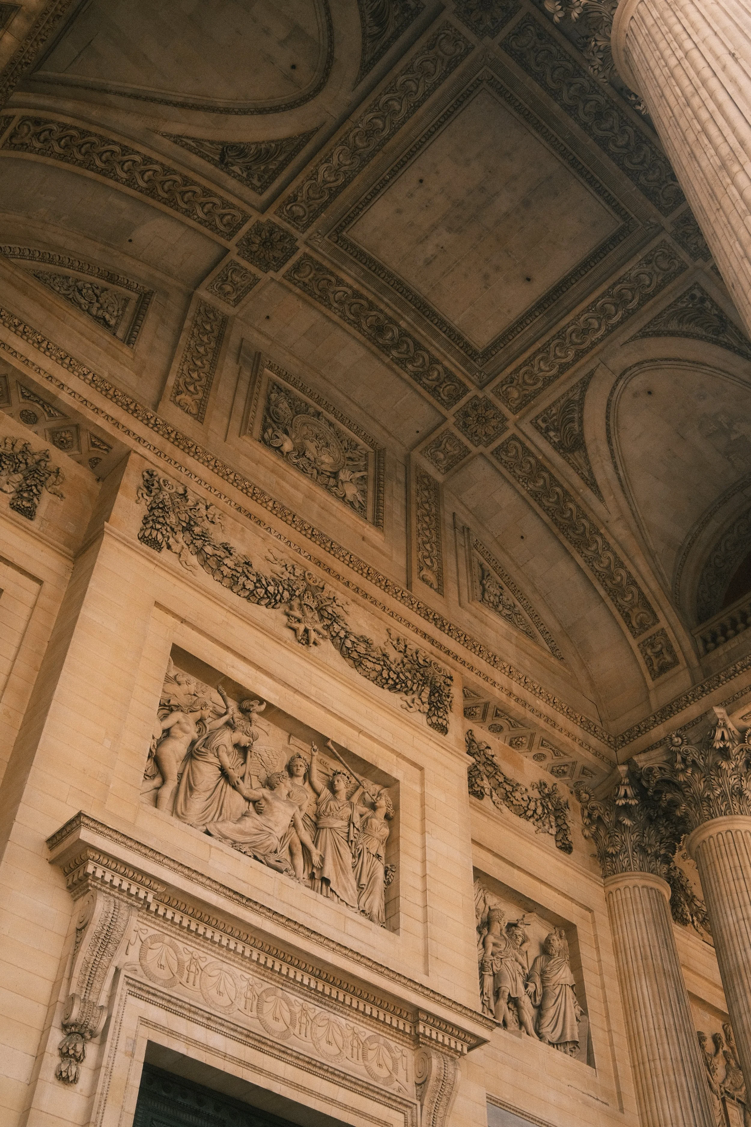 Close-up of ornate classical architectural elements including intricate friezes, bas-relief sculptures of historical figures, and decorative moldings on a historic building interior with Corinthian columns.