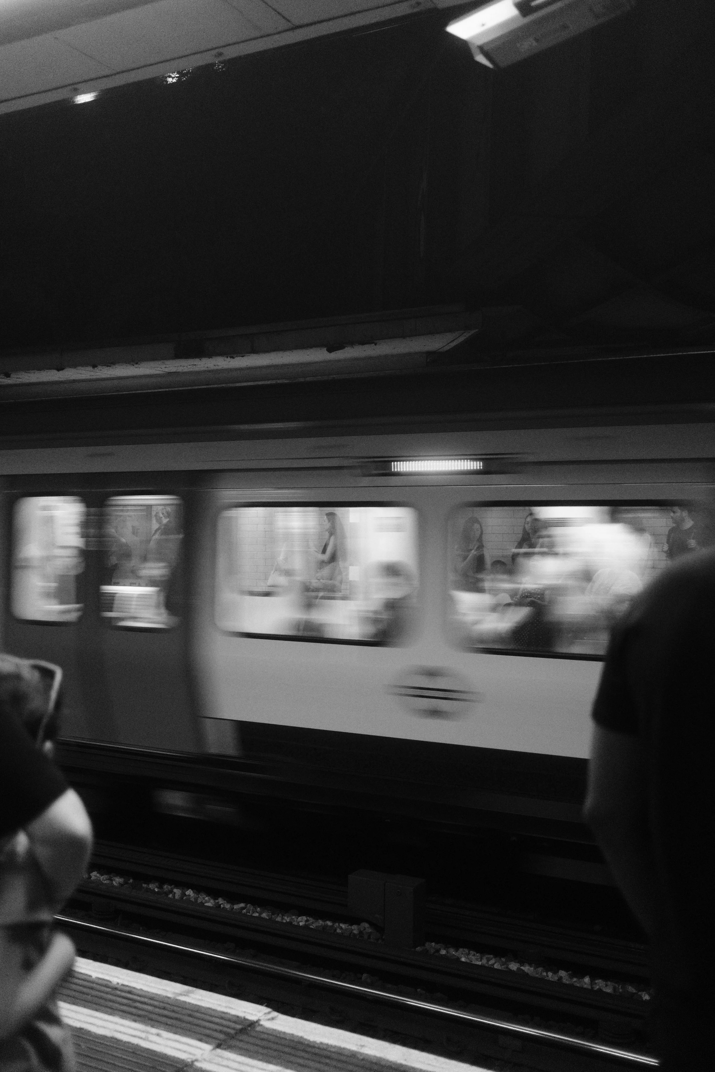A subway train moving through a station with blurred passengers visible inside, captured in black and white.