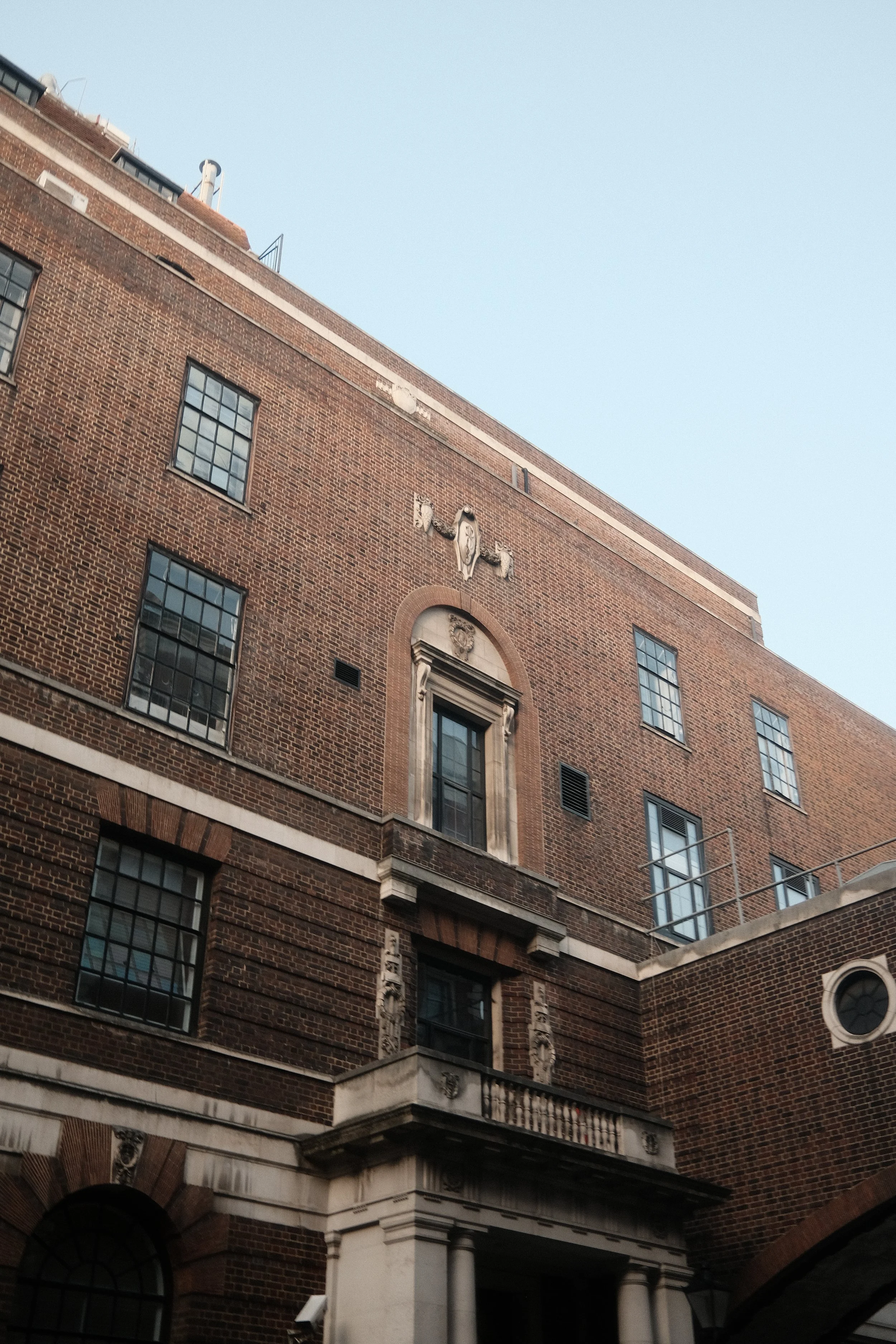 A multi-story brick building with decorative architectural features and large windows, under a clear blue sky.