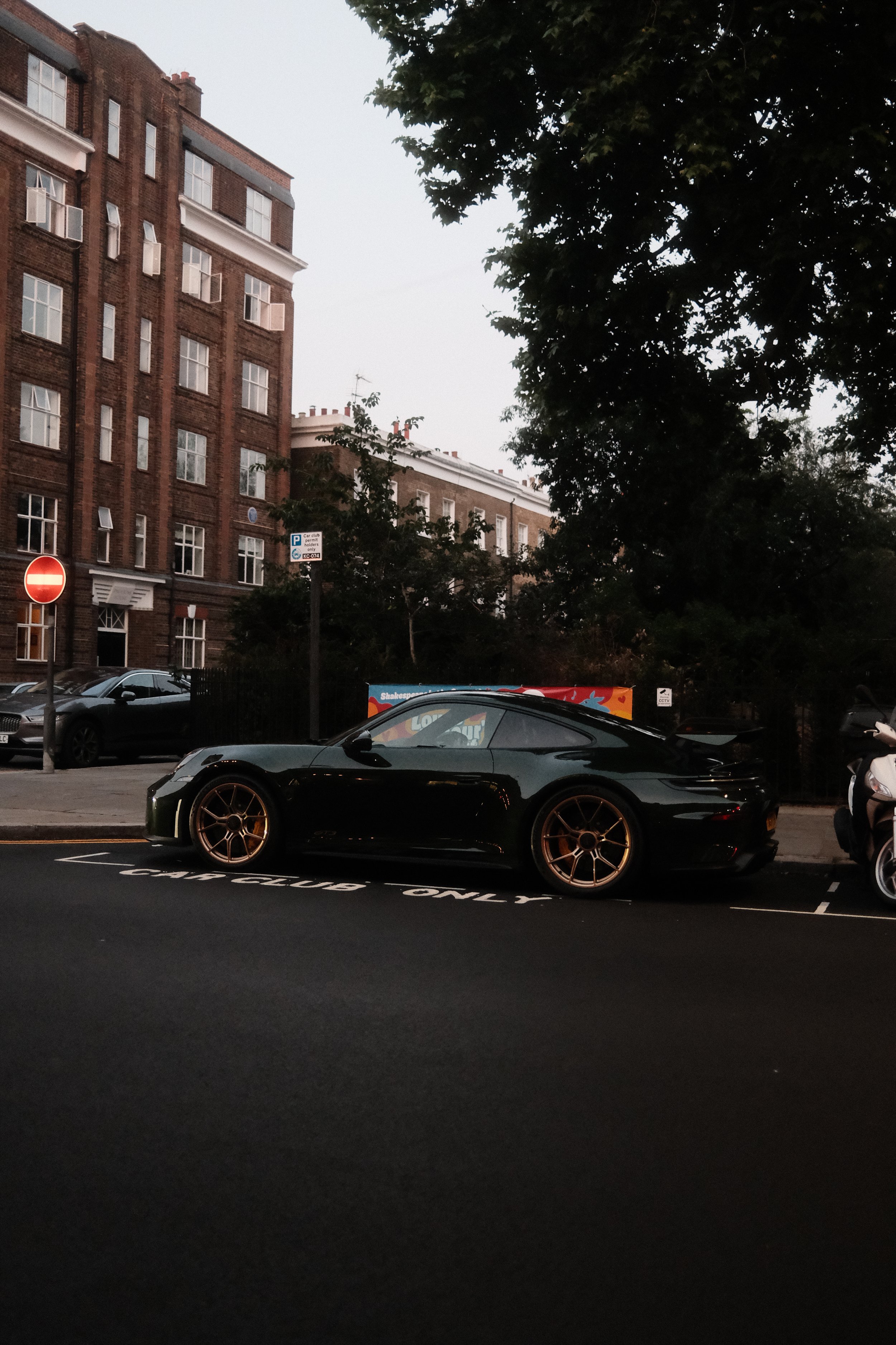 A black sports car parked in a designated parking spot on a city street with buildings, trees, and parking signs in the background.