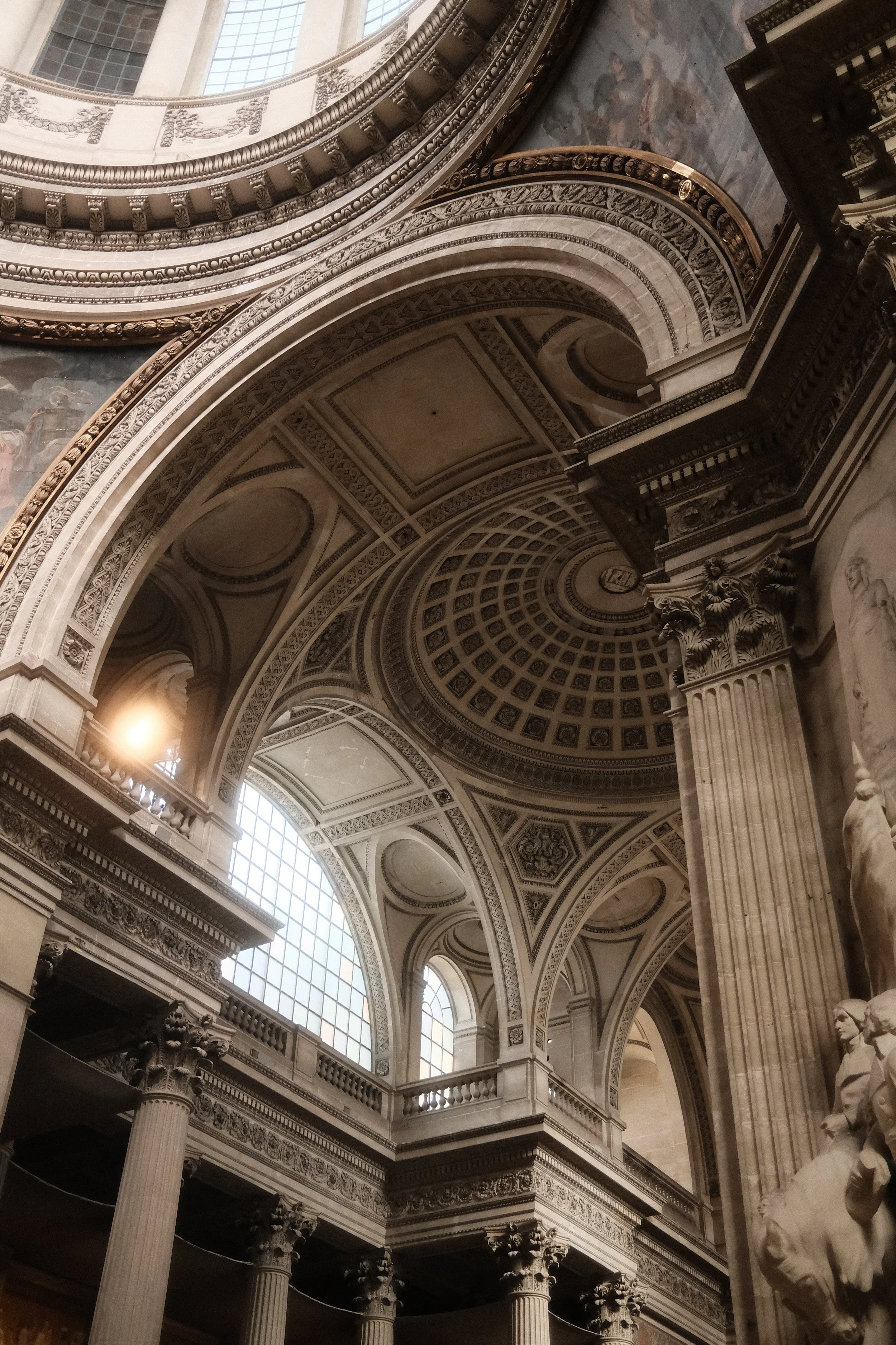 Interior view of a historic building with ornate arches, columns, intricate decorative details, and statues. Large windows allow natural light to illuminate the space.
