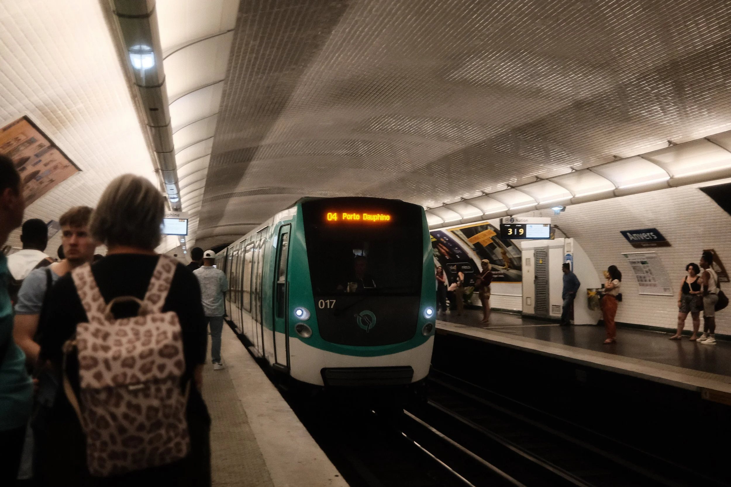 People waiting for a train at a subway station with a train on the platform. The train display shows it is heading to Porte Dauphine.