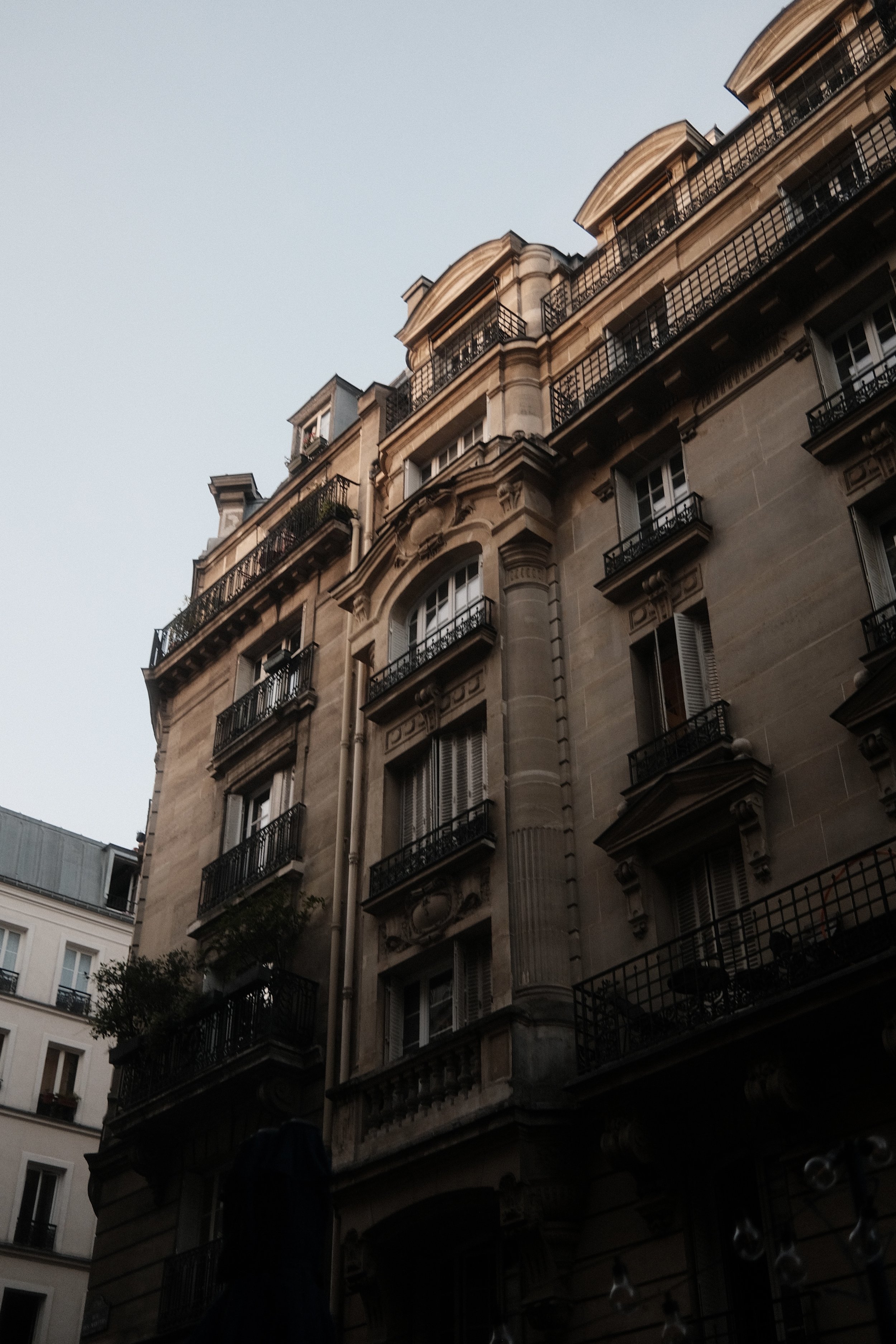 Parisian apartment building with ornate architecture, balconies, and tall windows, set against a clear sky.