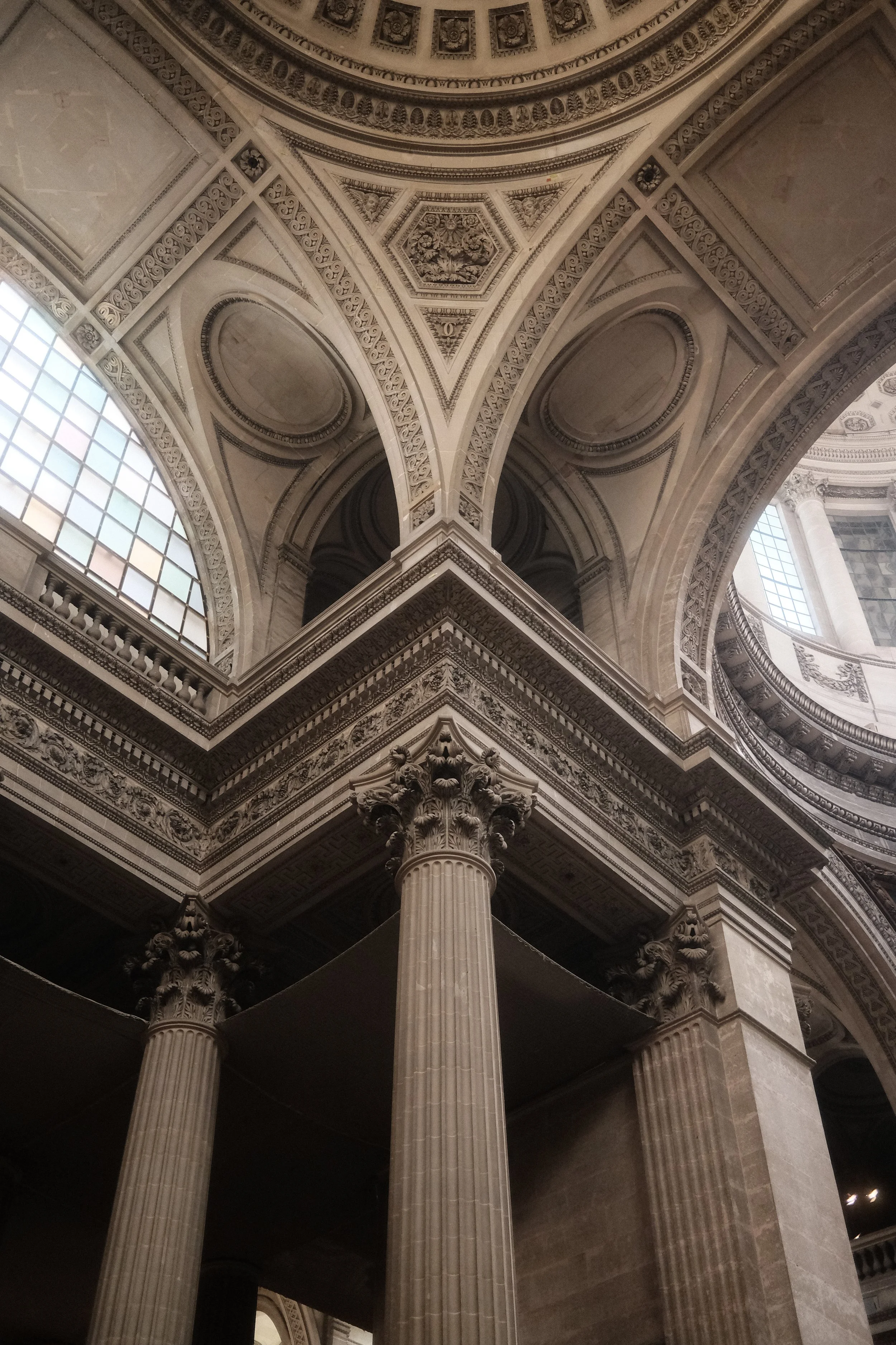 Interior view of a historic building featuring tall Corinthian columns, intricate decorative moldings, arched windows, and ornate ceiling details.